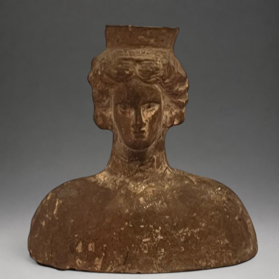 Female anthropomorphic oil lamp, Magna Graecia, 4th-3rd century BC.: Modeled and hollowed terracotta. Measures 11.5 x 11 x 4 cm. Oil lamp in the shape of a female bust, with an oval face, almond-shaped eyes, a straight nose, and full lips. The figure has wavy hair arra