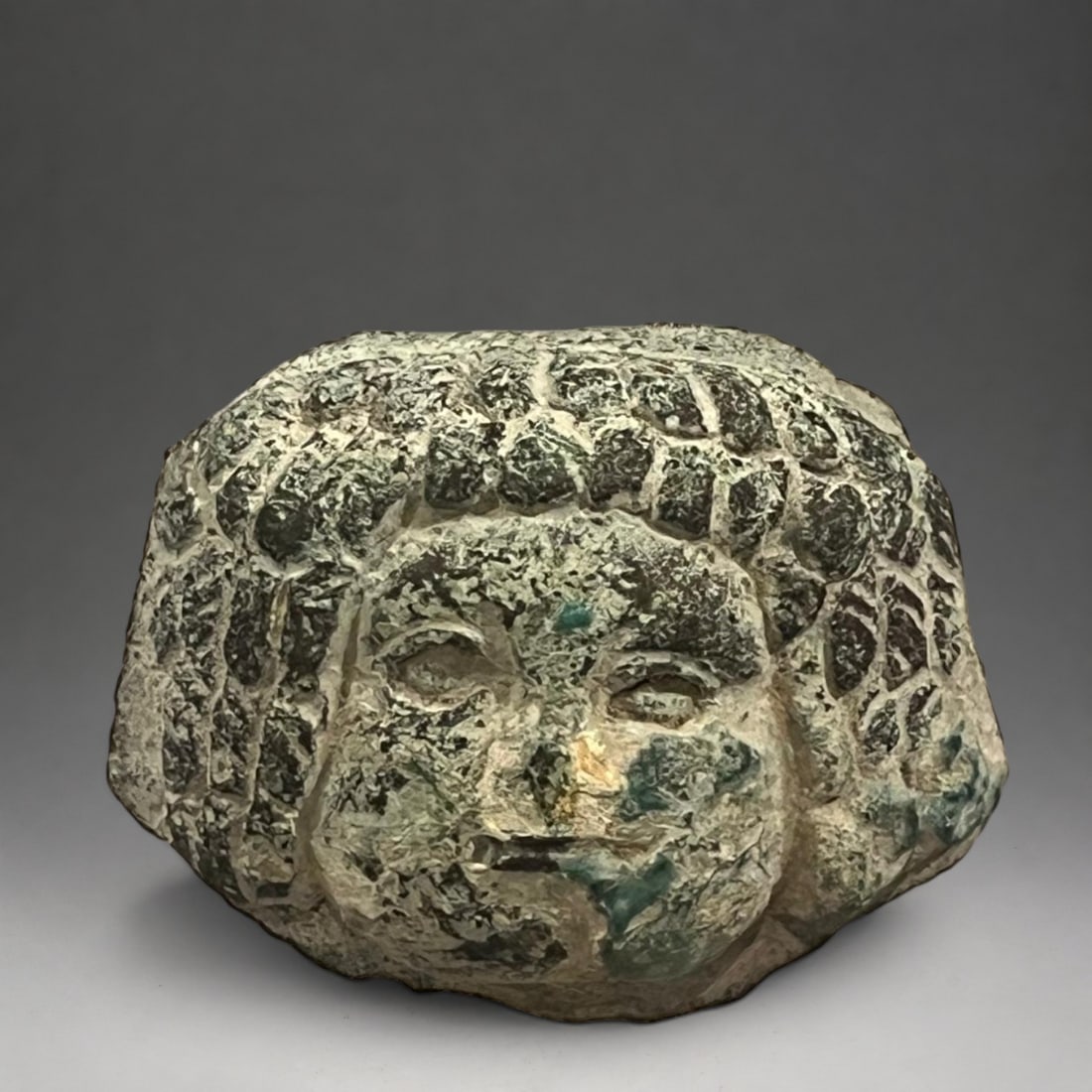 Celtic female head - 5th-4th century BC: Solid bronze with a greenish-gray patina and mineral oxidation. Measures 4 x 3 cm. Small female head with voluminous, twisted curls framing the face. It features prominent almond-shaped eyes, a define