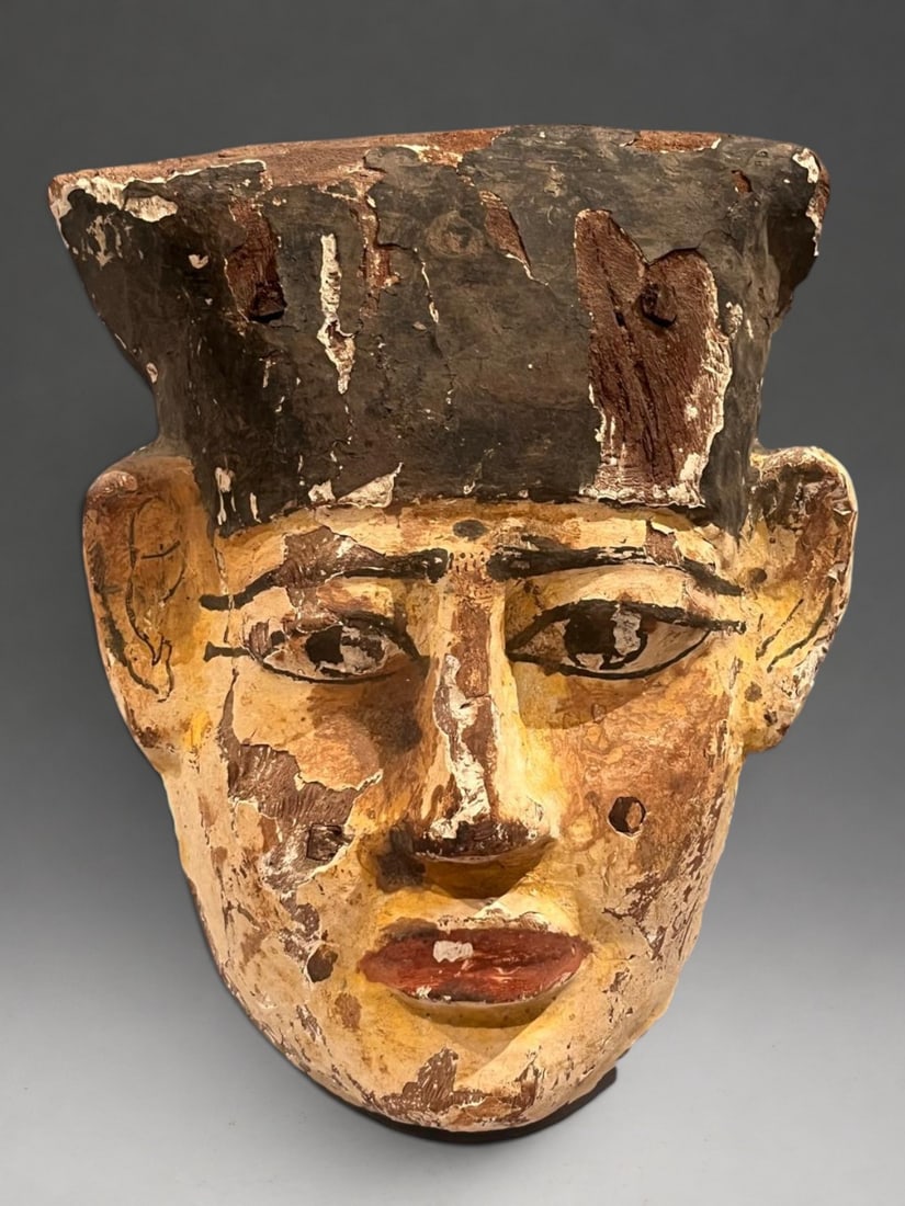 Polychrome Egyptian funerary mask, Egypt Late Period, 7th-4th century BC.: Polychrome wood with traces of gilding and mineral pigments. Measures 27 x 22 cm. Funerary mask with an idealized face, featuring red lips, rosy cheeks, almond-shaped eyes outlined in black, and arche