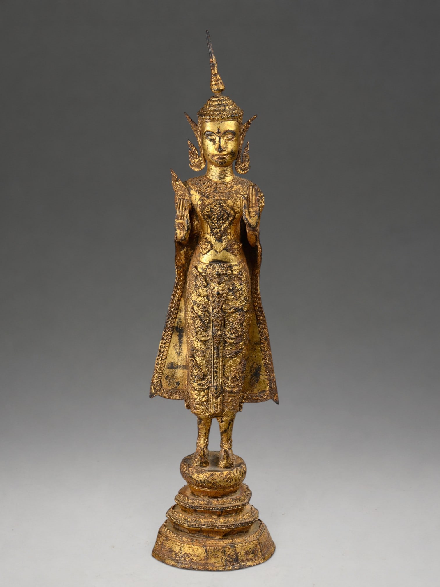 18th century Thai Buddha: Finely chased gilt bronze. Measures 71 cm in height. Figure of Buddha standing on a raised stepped base, hands in abhayamudra, and draped in a sumptuous utarasanga decorated with floral motifs and jew