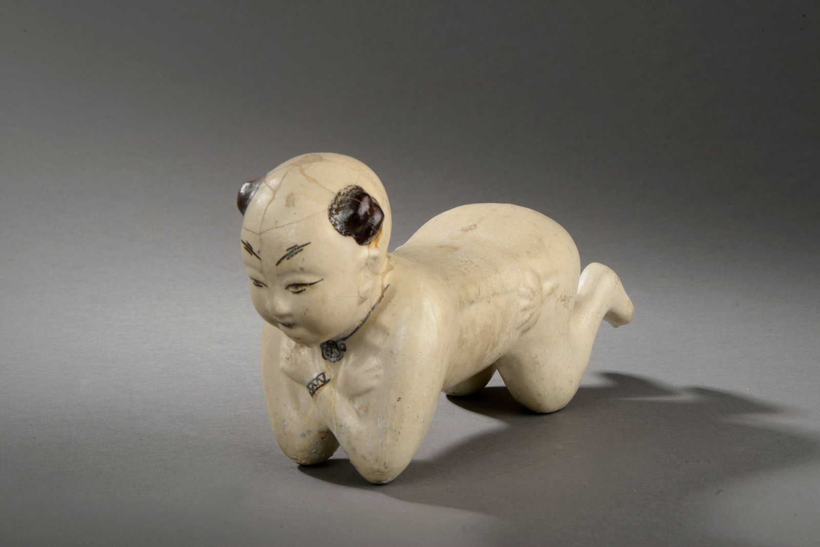 "Ho Ho", Chinese School, Song Dynasty, 10th-13th Century: Hand-modeled porcelain stoneware with cream slip and dark mineral pigments. Dimensions not indicated. Ceramic sculpture depicting one of the "Ho Ho" twins in a reclining position, with arms crossed un