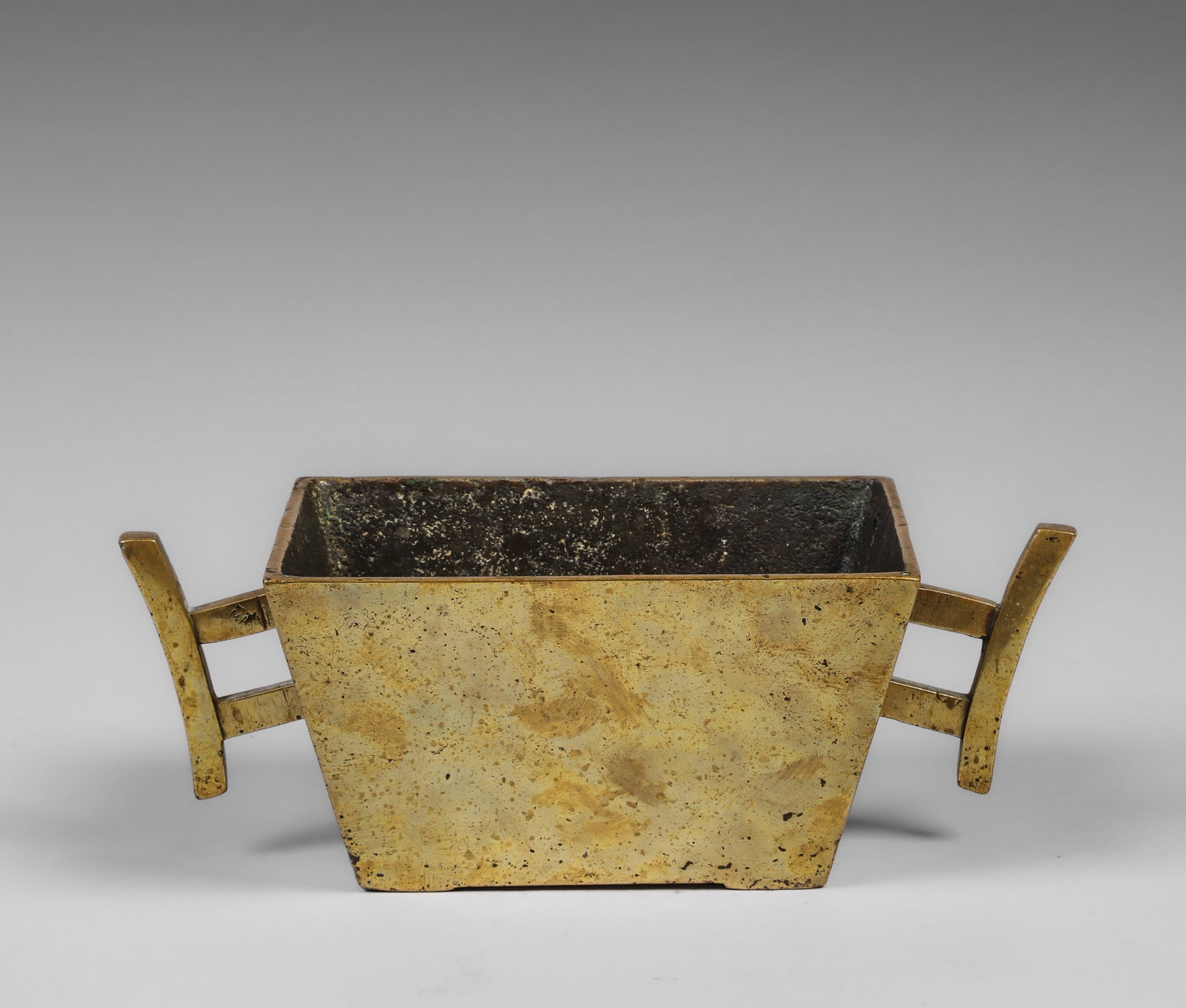Square incense burner with side handles, Qing Dynasty Chinese school, 19th century: Cast and patinated gilt bronze. Measures 9 x 24.5 x 16 x 12 cm. Incense burner with a slightly trapezoidal, quadrangular structure and two geometric side handles that visually extend the piece's horiz