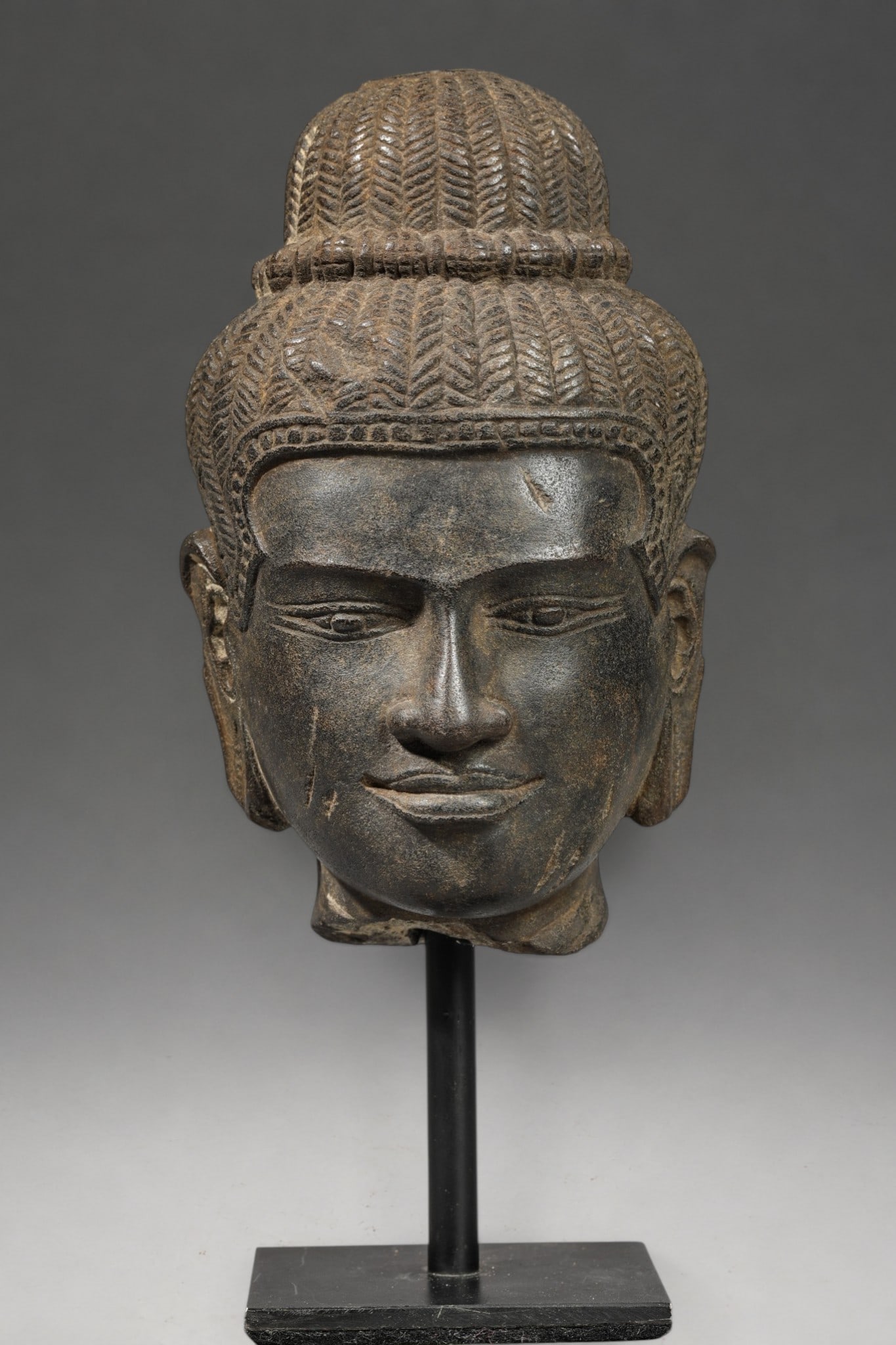Shiva head, Khmer Baphuôn school, 11th century: Beige stoneware with a dark patina. Measures 16 cm in height. Shiva head with a youthful face, soft features, slightly hollowed-out almond-shaped eyes, and lips in a slight smile. The hair is braided 