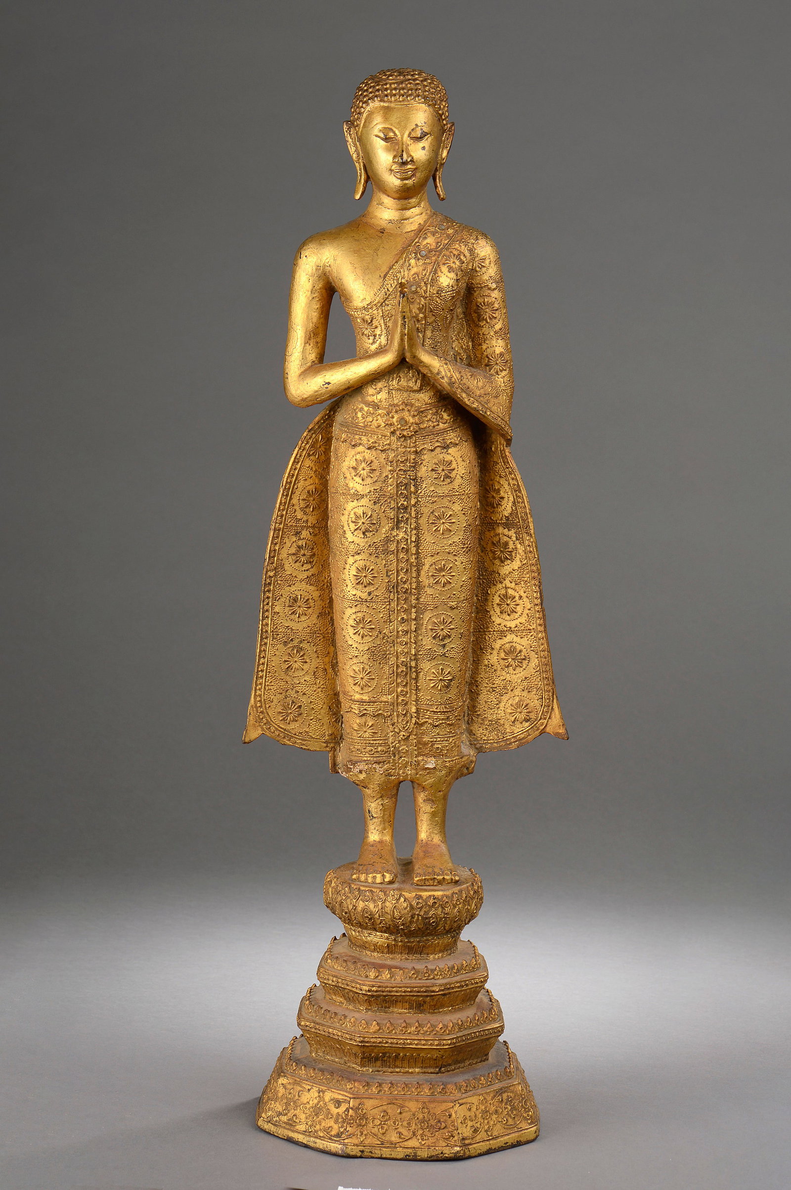 Buddha worshipper in anjali mudra, Kingdom of Ratanakosin, 19th-20th century: Gilded bronze, chased. Measures 61 cm in height. Figure of Buddha standing on a stepped base, with hands joined in anjali mudra in a gesture of veneration and spiritual contemplation. The figure wears