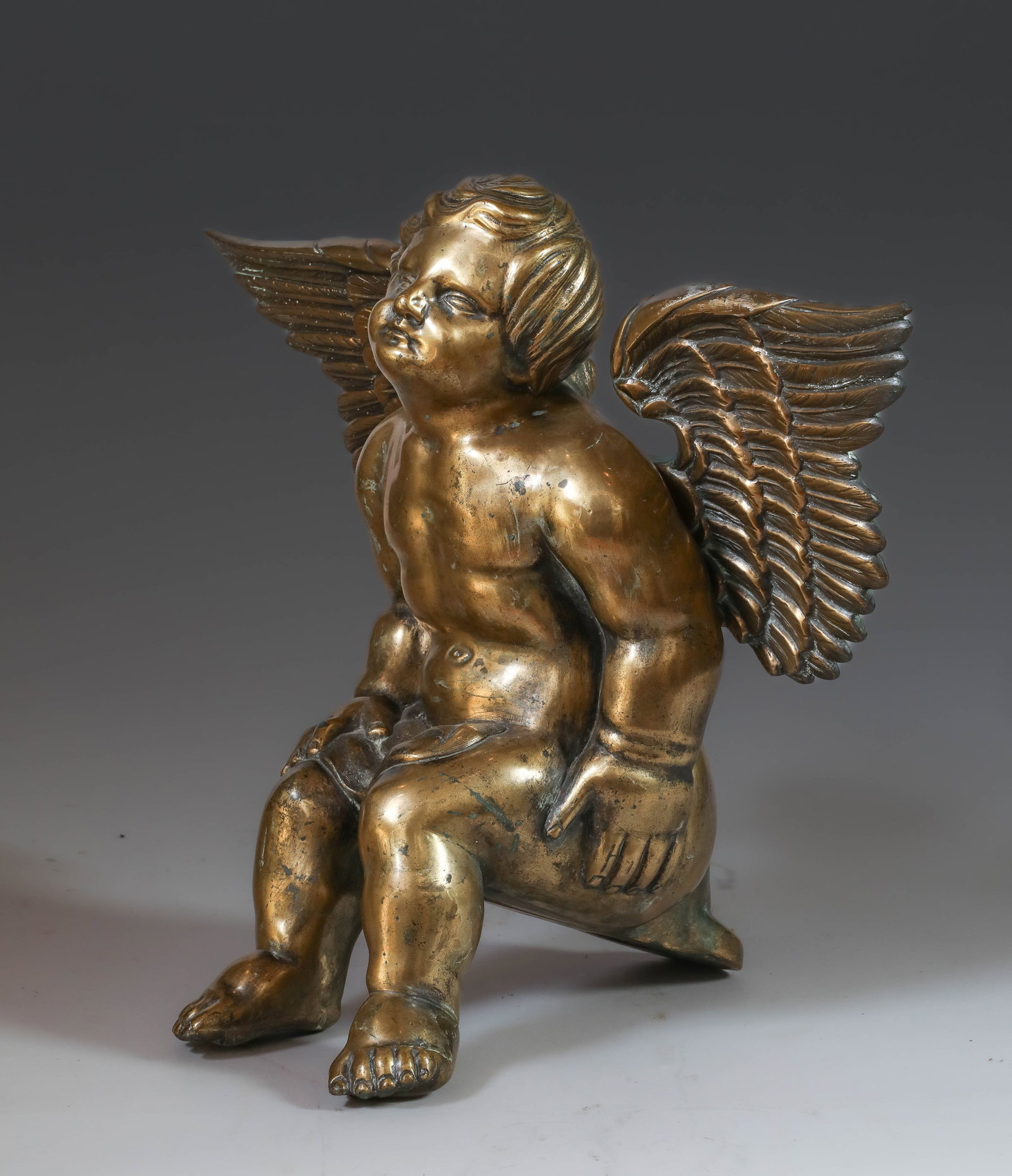 Seated angel with outstretched wings, France, 17th century: Gilded bronze. Measures 43 x 54 cm. Angel depicted seated with wings fully extended, muscular physique, and a draped cloak partially draped over the legs. The figure exhibits a dynamic and expressive 
