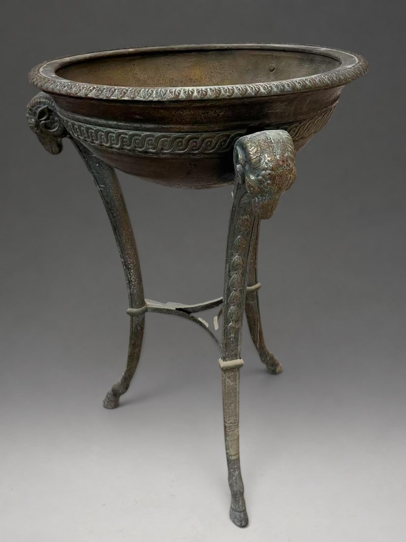 Exceptional Neoclassical bronze planter, early 19th century: Bronze with a brown patina tinged with green. Measures 89 x 56 cm. Circular basin with an open profile, supported by three curved legs joined by a triangular spacer. The basin features a wide molded r