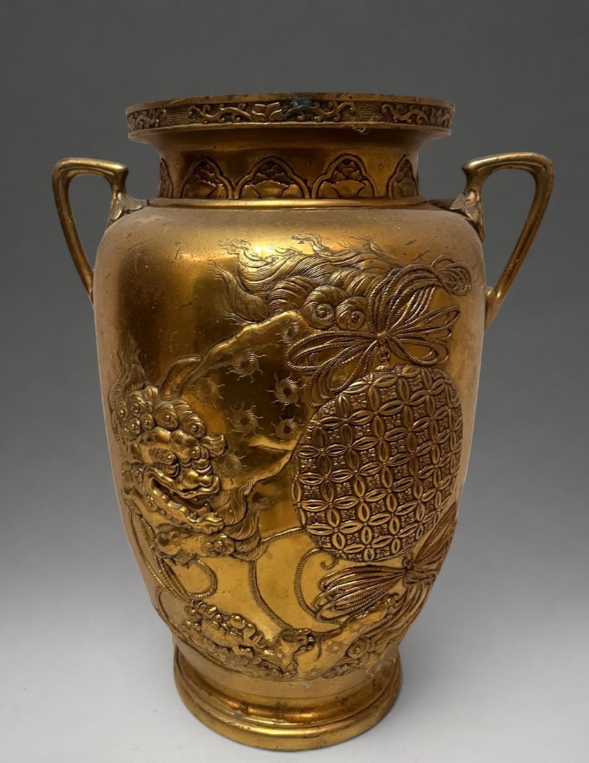 Vase with handles and shishi decoration, Japan, Meiji period, 19th - 20th century: Chiseled bronze or gilt brass. Measures 37 x 18 cm. Baluster-bodied vase with two side handles and a flared neck decorated with a vegetal frieze. The body features relief figures of shishi fish amid u