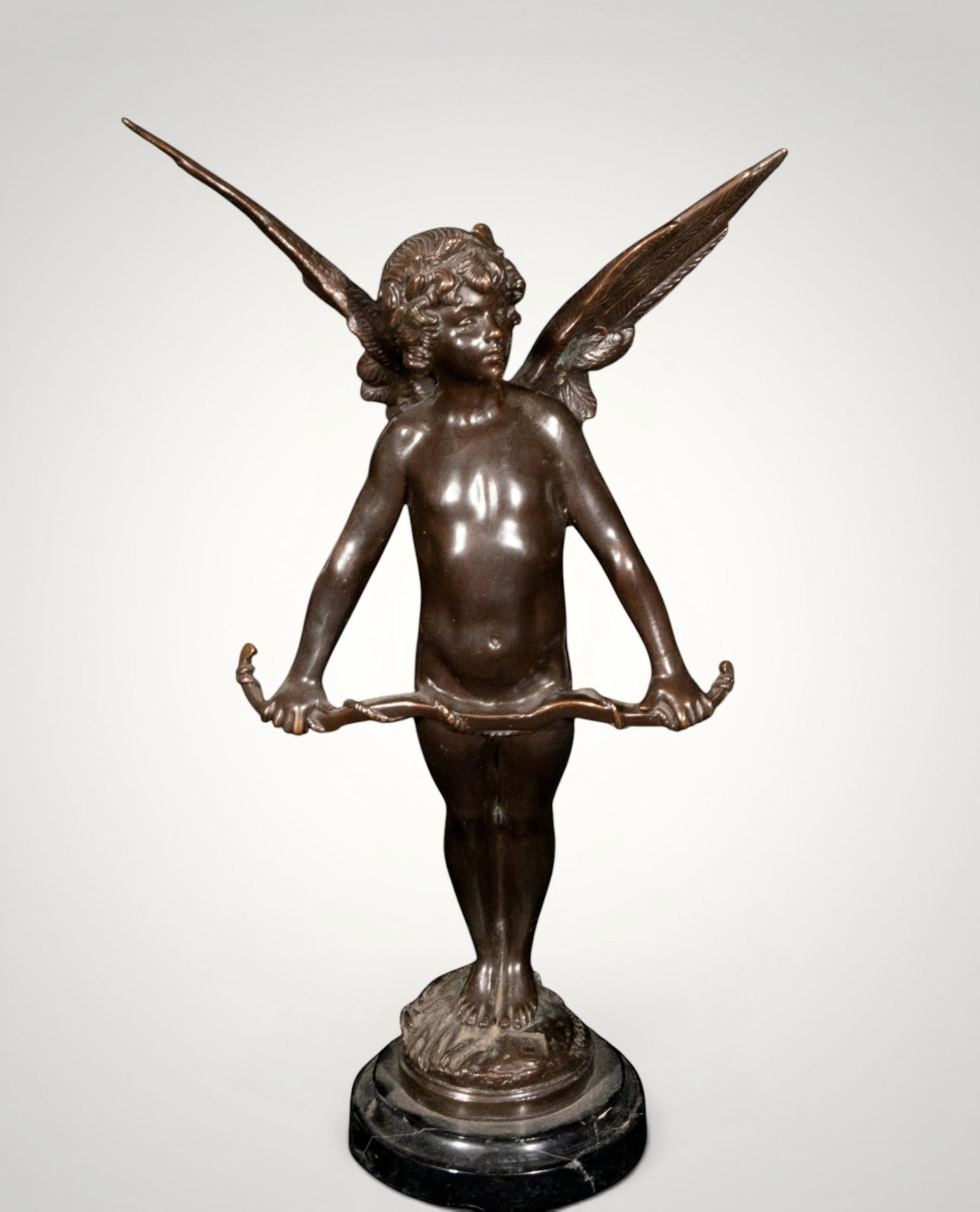 Cupid with bow. European school. 19th century: Patinated bronze on a marble base. Measures 44 x 26 x 13 cm. Winged figure of Cupid holding a bow, arranged frontally on a circular base. The idealized childlike anatomy, the spread wings, and the pol