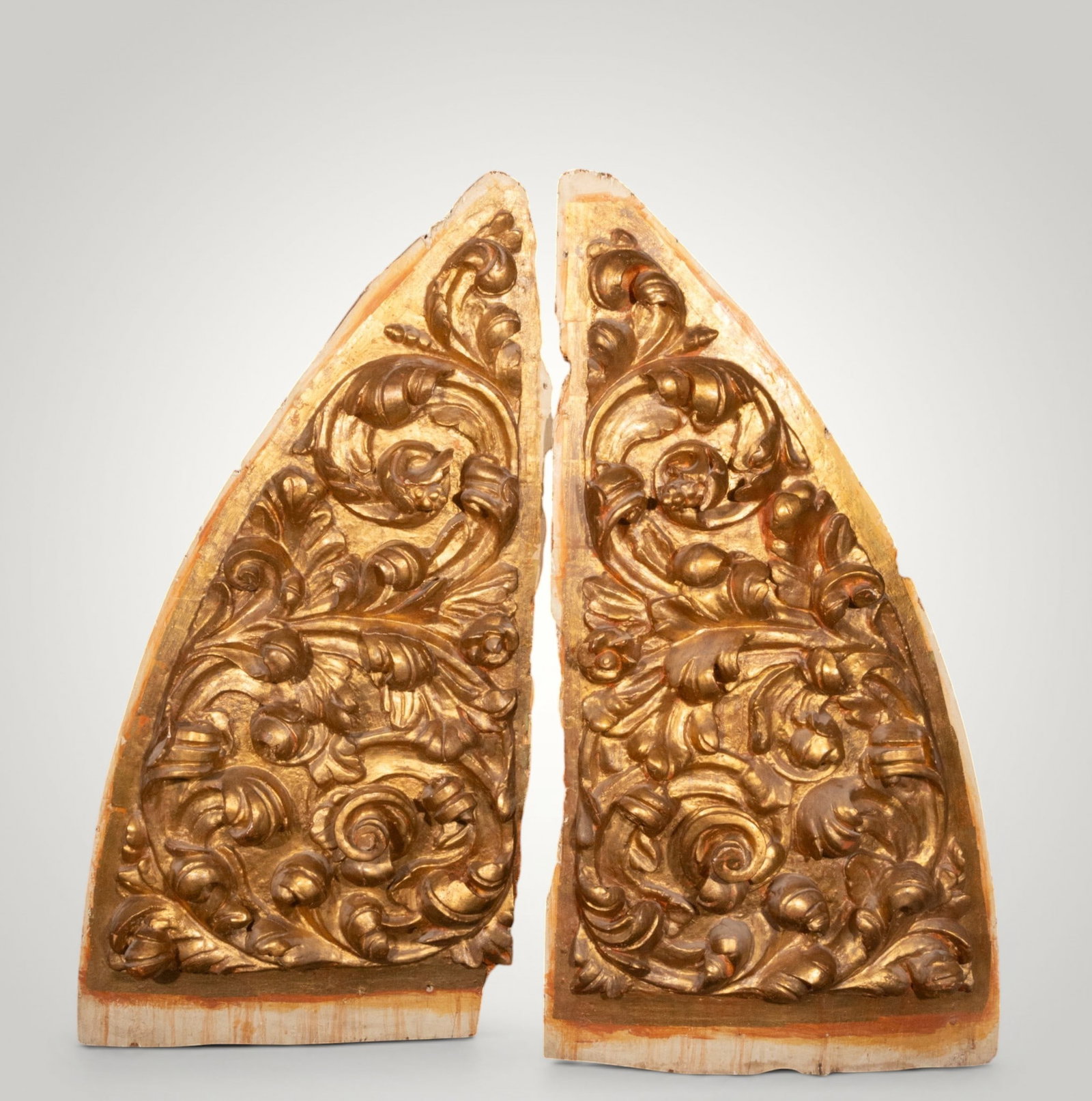 Pair of ornamental panels with scrollwork. Hispanic School. 18th century: Carved and gilded wood. Measures 114 x 57 cm. Pair of pointed-profile panels decorated with dense vegetal scrolls, leaves, and fruit in relief. The deep carving, symmetrical rhythm, and warm gilding a