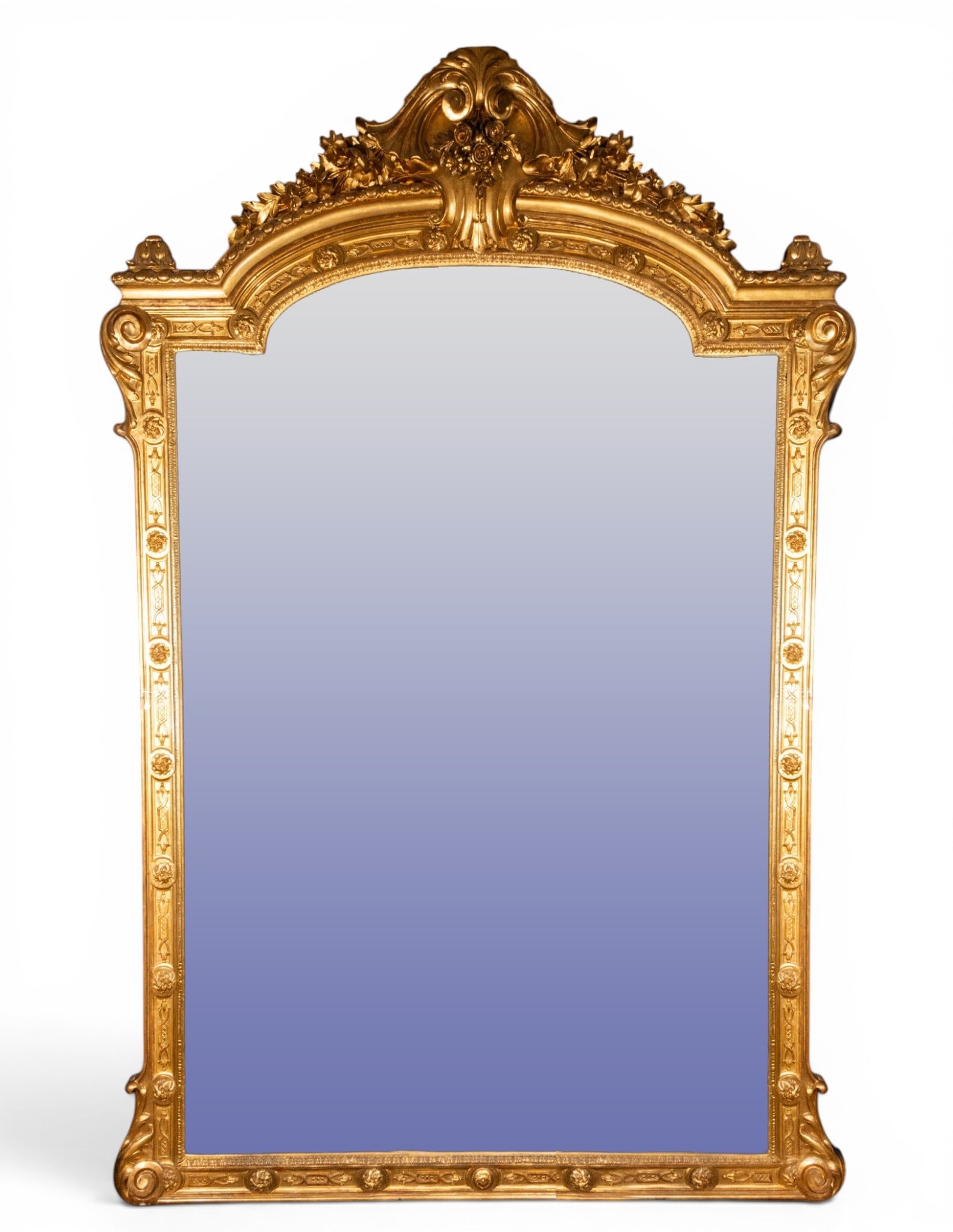 Monumental mirror with floral crest. European School. 18th-19th centuries: Carved and gilded wood with mirror. Measures 253 x 161 cm. Large-format mirror with a curved finial, floral garlands, scrolls, and a central medallion. The palatial scale, meticulous carving, and bril