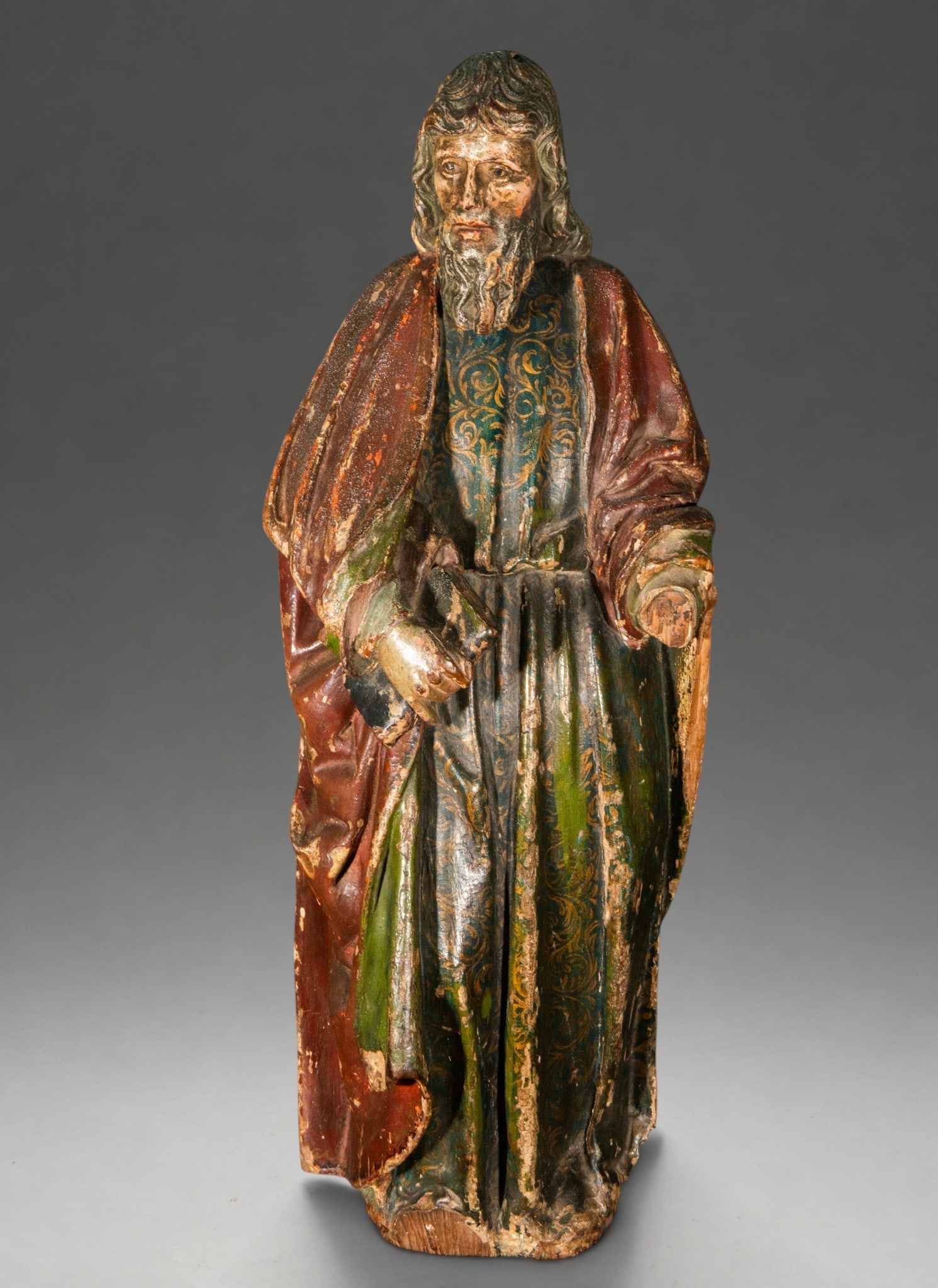 Romanist Saint of the late 16th century – Spanish School: Polychrome wood carving. Dimensions: 69 × 28 × 20 cm. Standing bearded male figure, dressed in a tunic decorated with gold motifs and a wide reddish cloak. It retains traces of green, red, blue, and