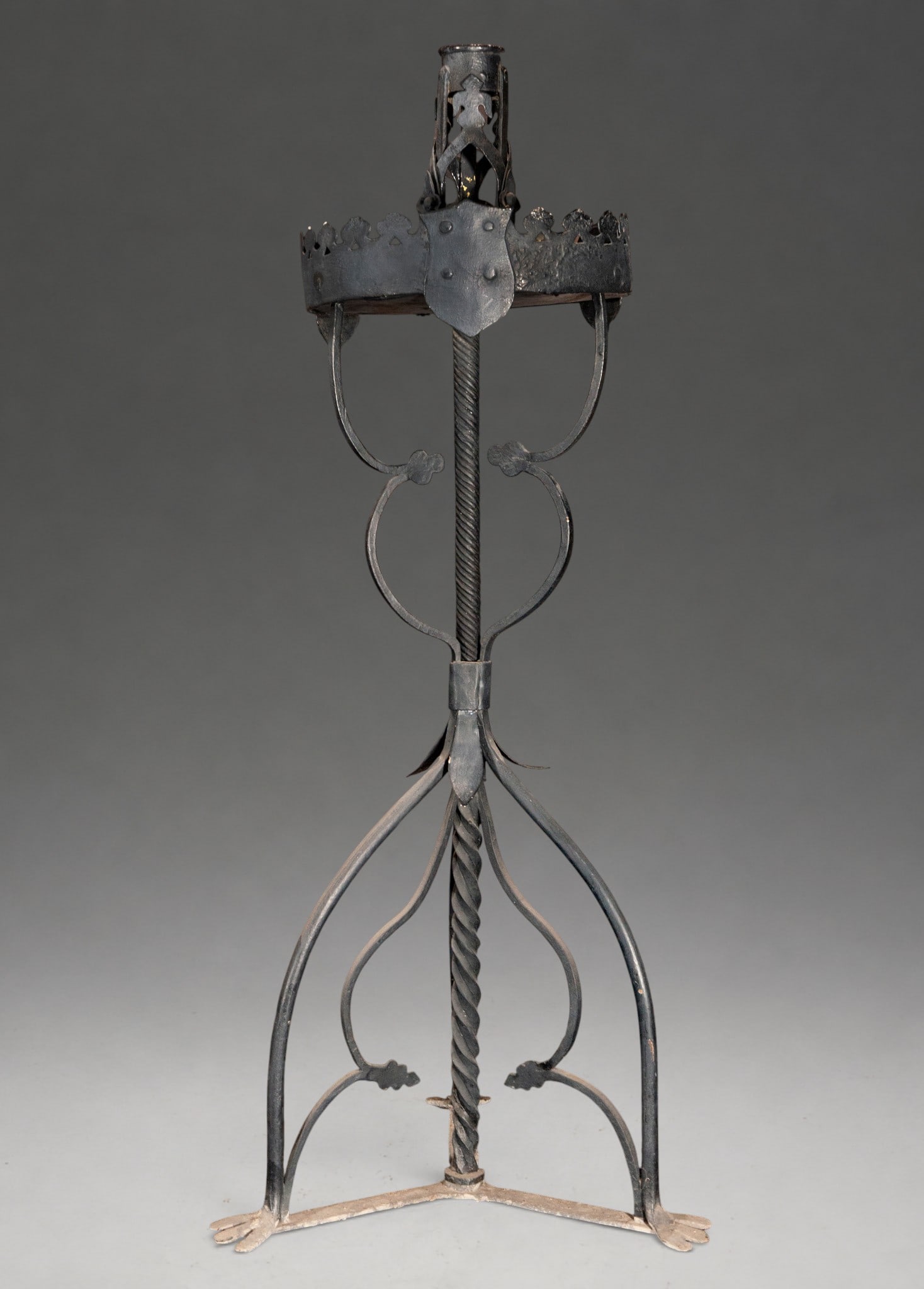 Wrought iron floor candlestick – 17th century: Standing candlestick made of wrought iron. Dimensions: 113 × 48 × 43 cm. Twisted central shaft, tripartite structure with curved supports and cut-out decoration inspired by plants. Circular upper se