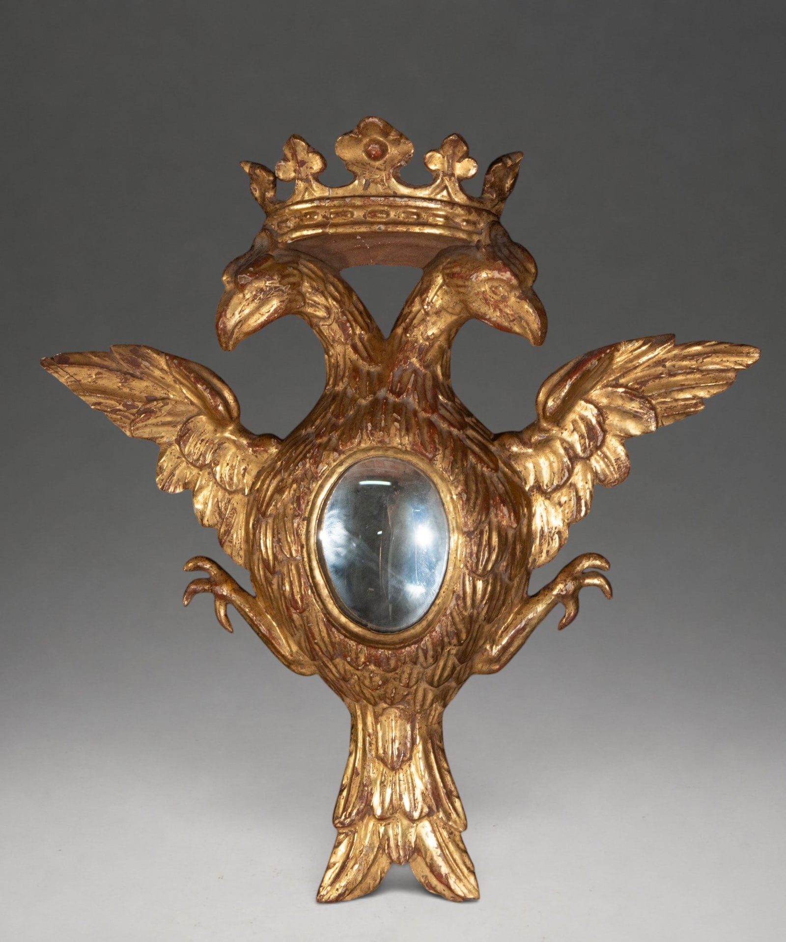 Carved and gilded wooden mirror with crowned double-headed eagle – 19th century: Carved and gilded wooden mirror depicting a crowned double-headed eagle with outstretched wings and a small oval mirror in the center of its body. Dimensions: 42 × 41 × 8 cm. The gilding shows wear,