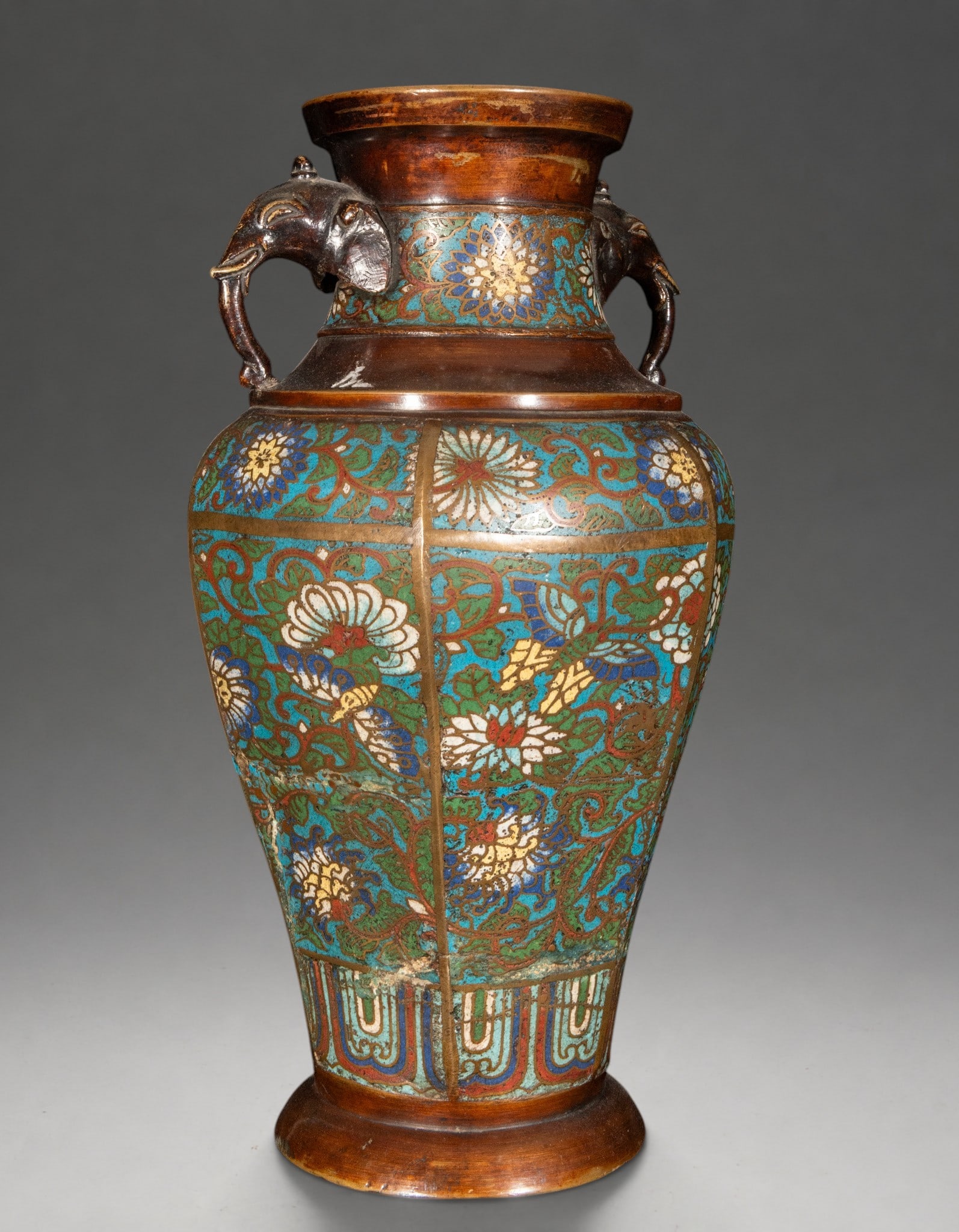 Vase with elephant handles – China – 19th century: Bronze jar decorated with cloisonne enamel, with an ovoid body and short neck, featuring two lateral handles modeled as elephant heads. The decoration is arranged in registers with flowers and vegetal