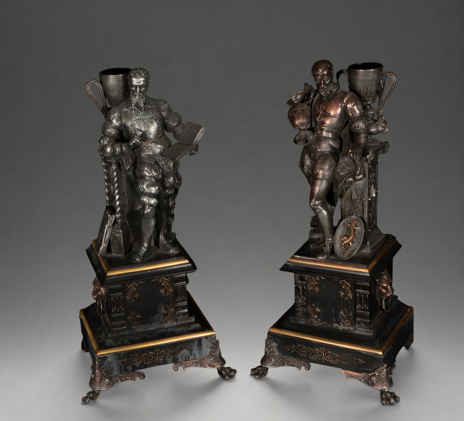Pair of allegorical figures of the Arts – 19th century: Pair of patinated metal sculptures, probably pewter or a similar alloy, depicting male figures in Renaissance attire associated with the Arts and Letters. One figure holds an open book, while the othe
