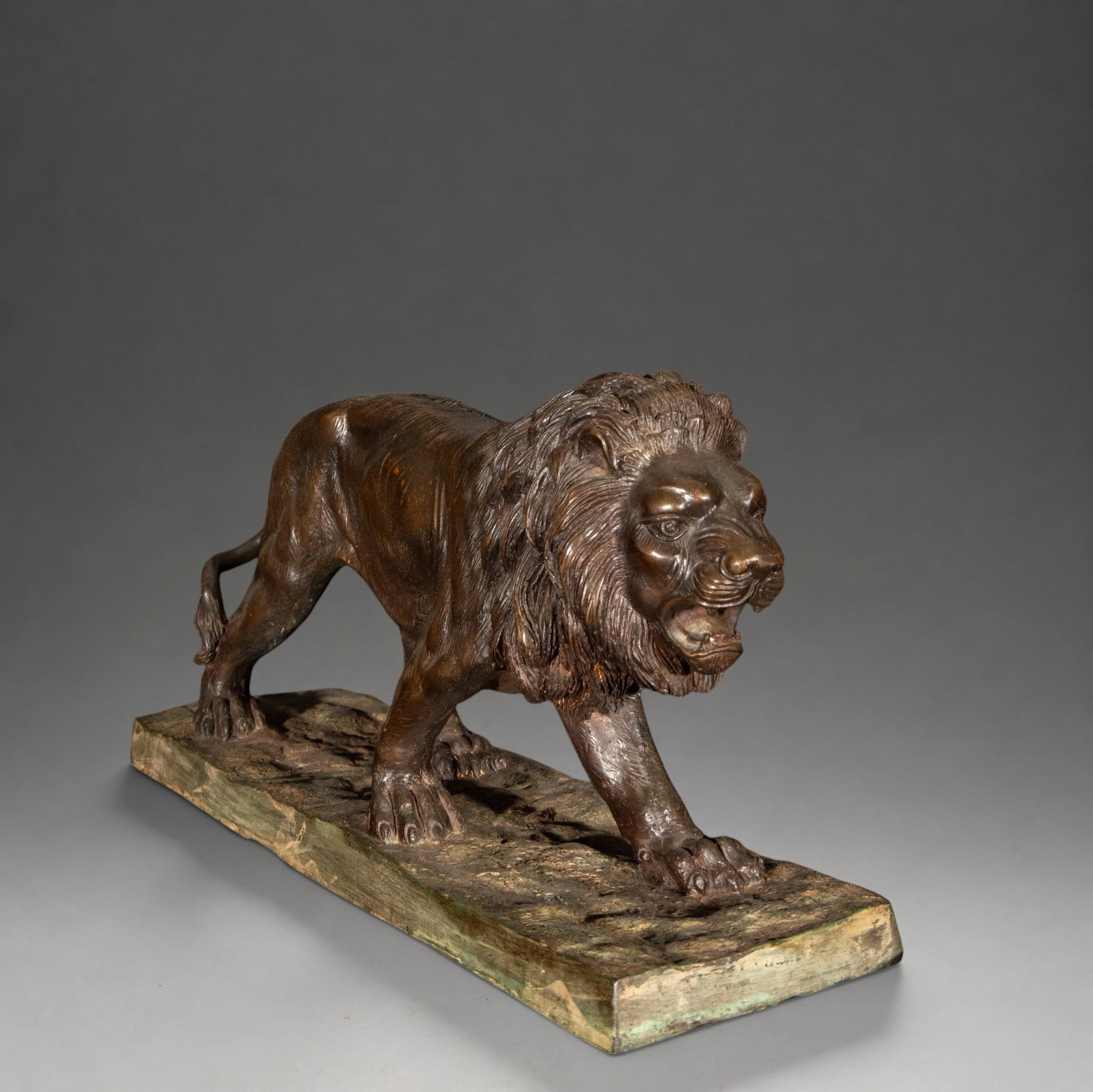 Roaring Lion – late 19th/early 20th century: Patinated bronze sculpture depicting a lion in motion, with open jaws and a richly detailed mane. The figure stands on a rectangular base with a rocky surface. According to the existing record, it was