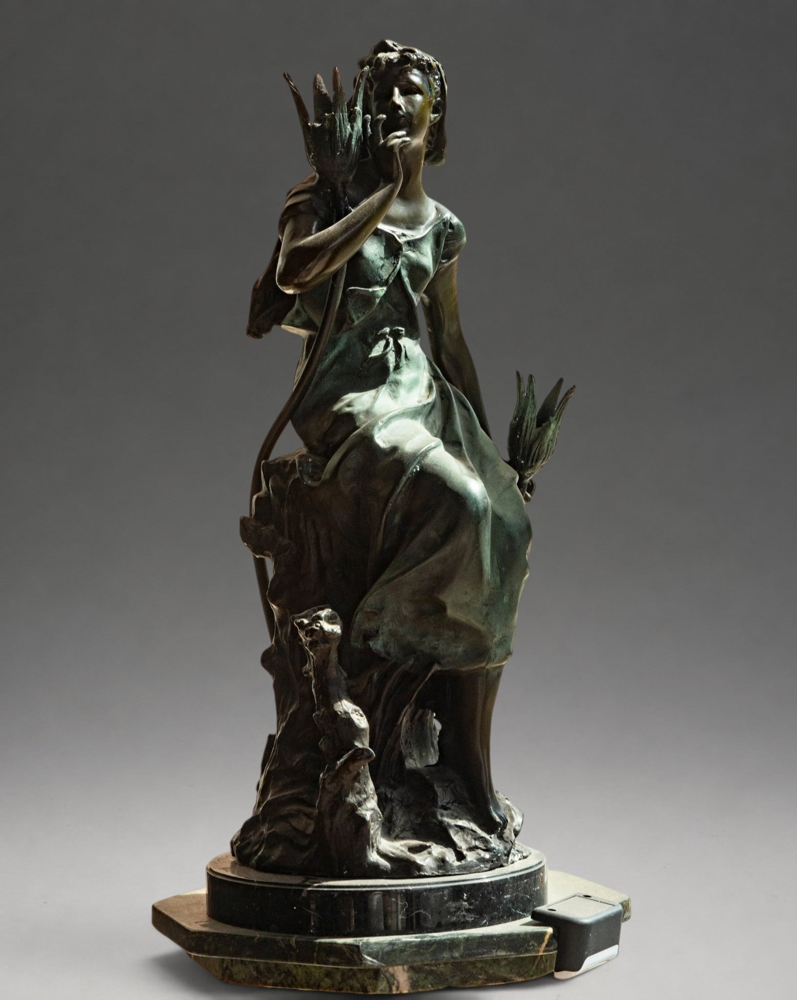 Female figure seated among vegetation, signed – late 19th-early 20th century: Patinated bronze sculpture depicting a seated young woman in a naturalistic setting, dressed in a long tunic and cloak, with one hand raised to her face. The figure is part of an allegorical compositi
