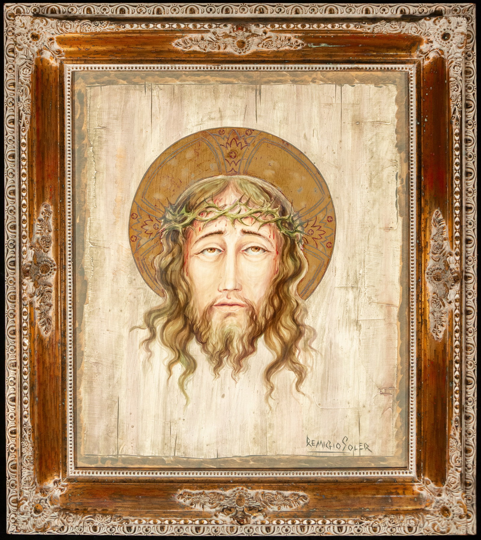 Holy Face, signed “Remigio Soler?? – Spanish School – second half of the 20th century: Oil on panel depicting the Holy Face of Christ, shown frontally with a crown of thorns and a decorated cruciform halo. The composition focuses the image against a light, textured background, highlight