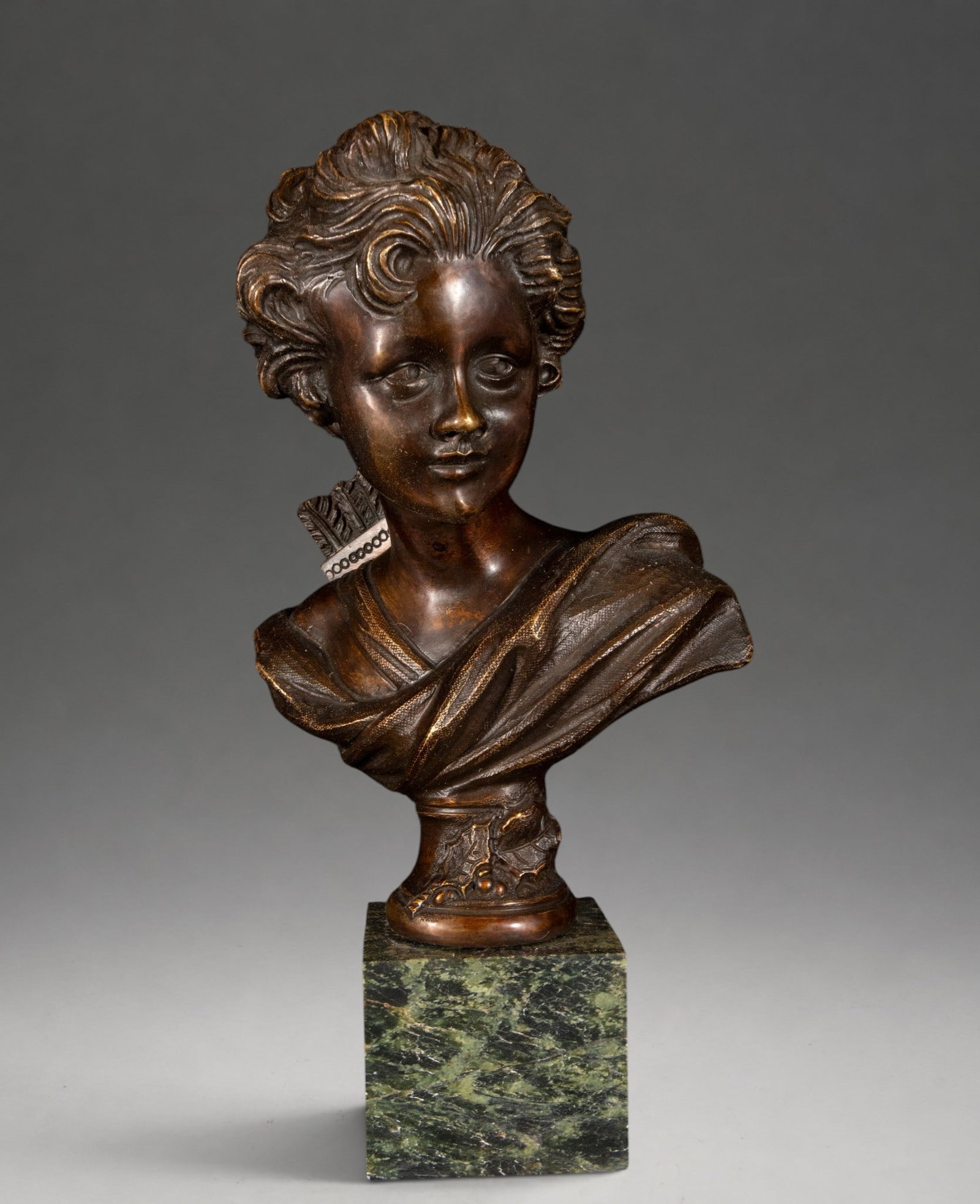 Diana the Huntress in bronze – late 19th/early 20th century: Patinated, cast, and chiseled bronze on a veined green marble base. Classical-inspired bust with flowing, wavy hair and draped clothing with abundant folds. Detailed modeling of hair and fabrics, with