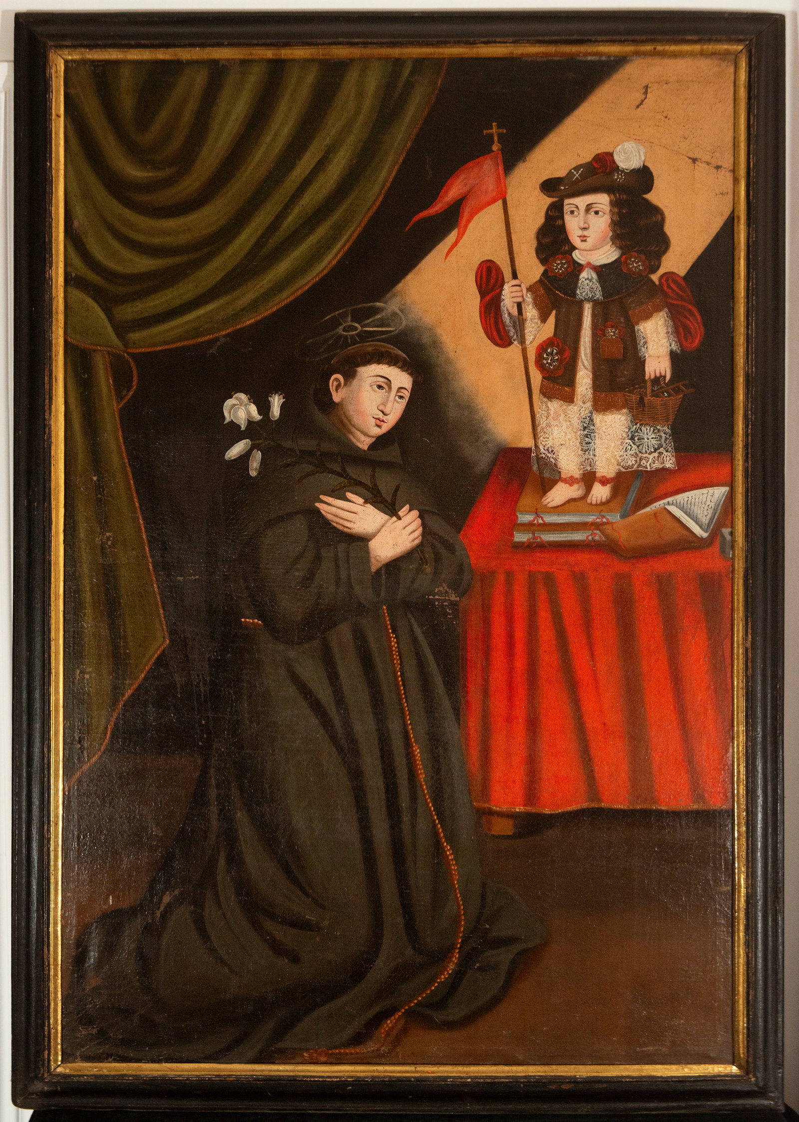Saint Anthony of Padua with the "Santo Menino" Jesus – Portuguese Colonial School – 17th-18th: Oil on canvas. Saint Anthony of Padua is depicted kneeling, dressed in a Franciscan habit, holding a staff of lilies and gazing at the Christ Child, who stands on a table dressed as a pilgrim, wearing