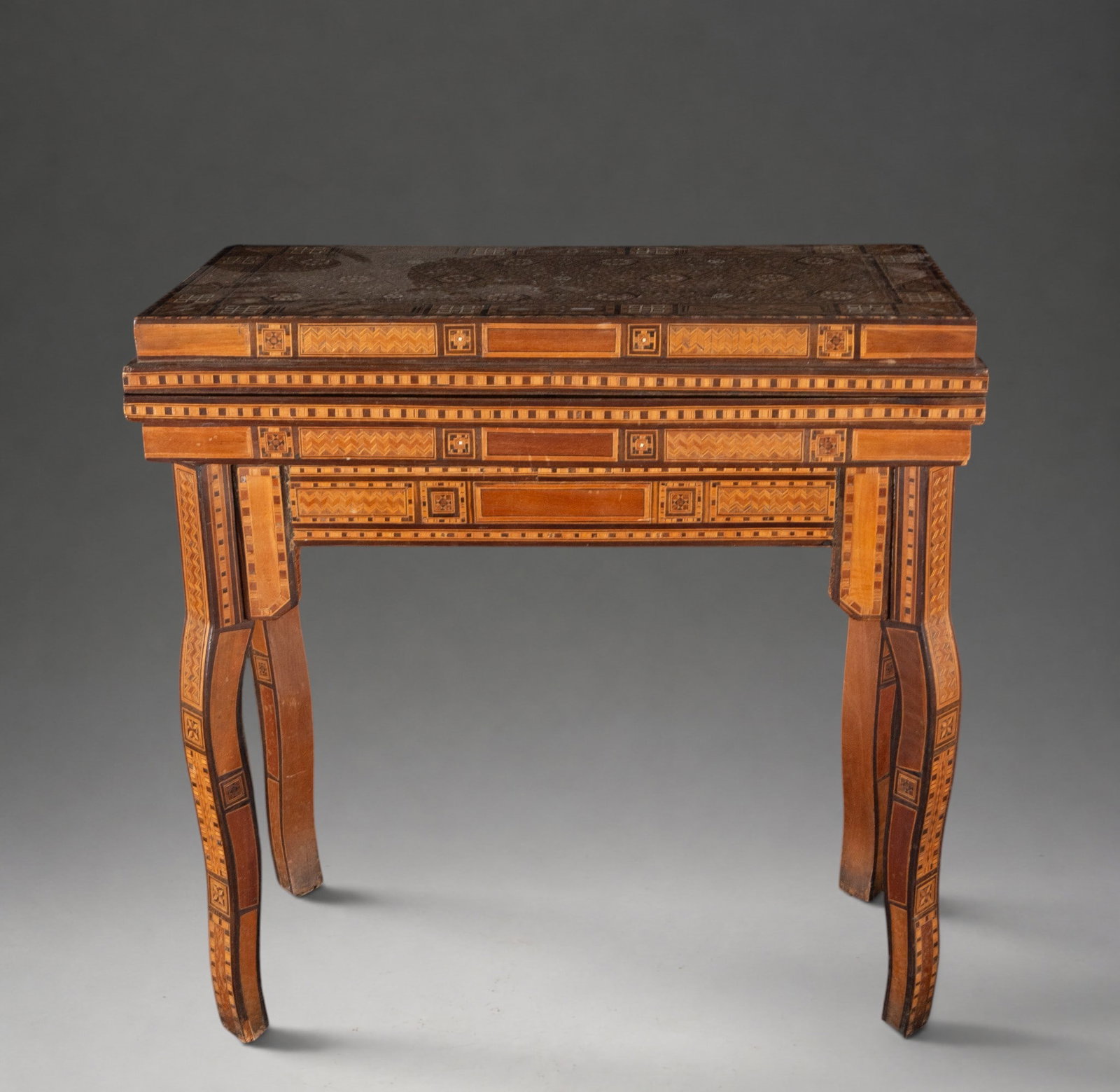 Moorish gaming table with marquetry and bone inlays – Oriental School – late 19th century: Wooden game table with rich geometric marquetry decoration and bone inlay, arranged in bands and repeating motifs on the top, apron, and legs. Oriental style. Dimensions: 62 x 62 x 31 cm.