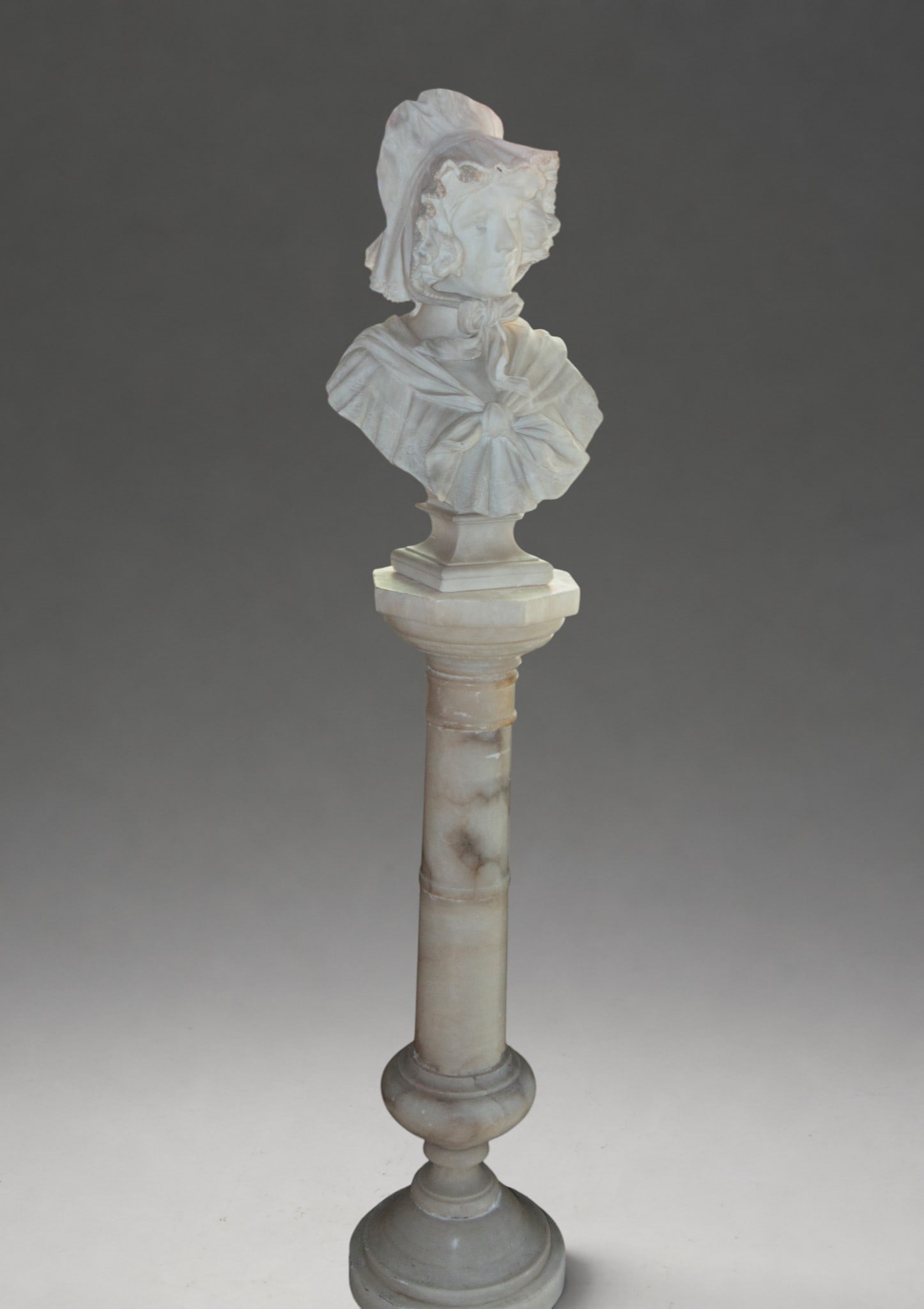Large French bust of a Belle Éporque lady in marble, late 19th century: Female bust carved in white marble with an alabaster base, depicting a young woman with a wide-brimmed hat and a scarf tied around her neck, displayed on a tall alabaster pedestal. Detailed treatment 