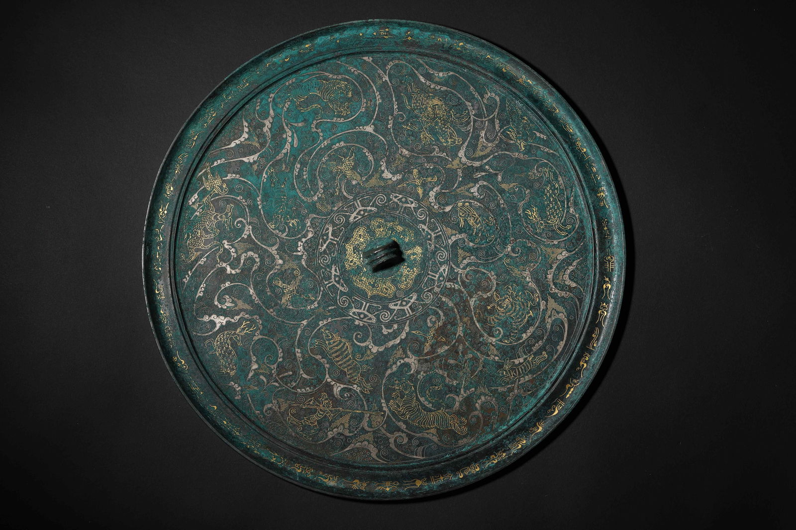 Warring states period gold-and-silver-inlaid mythical beast-pattern bronze mirror: C. 475-221 Bce. Bronze body with cuo-jin & silver coiled dragon & cloud patterns; Gold-white decorations stand out clearly against the teal-brown background. Dynamic & precise patterns. A top example