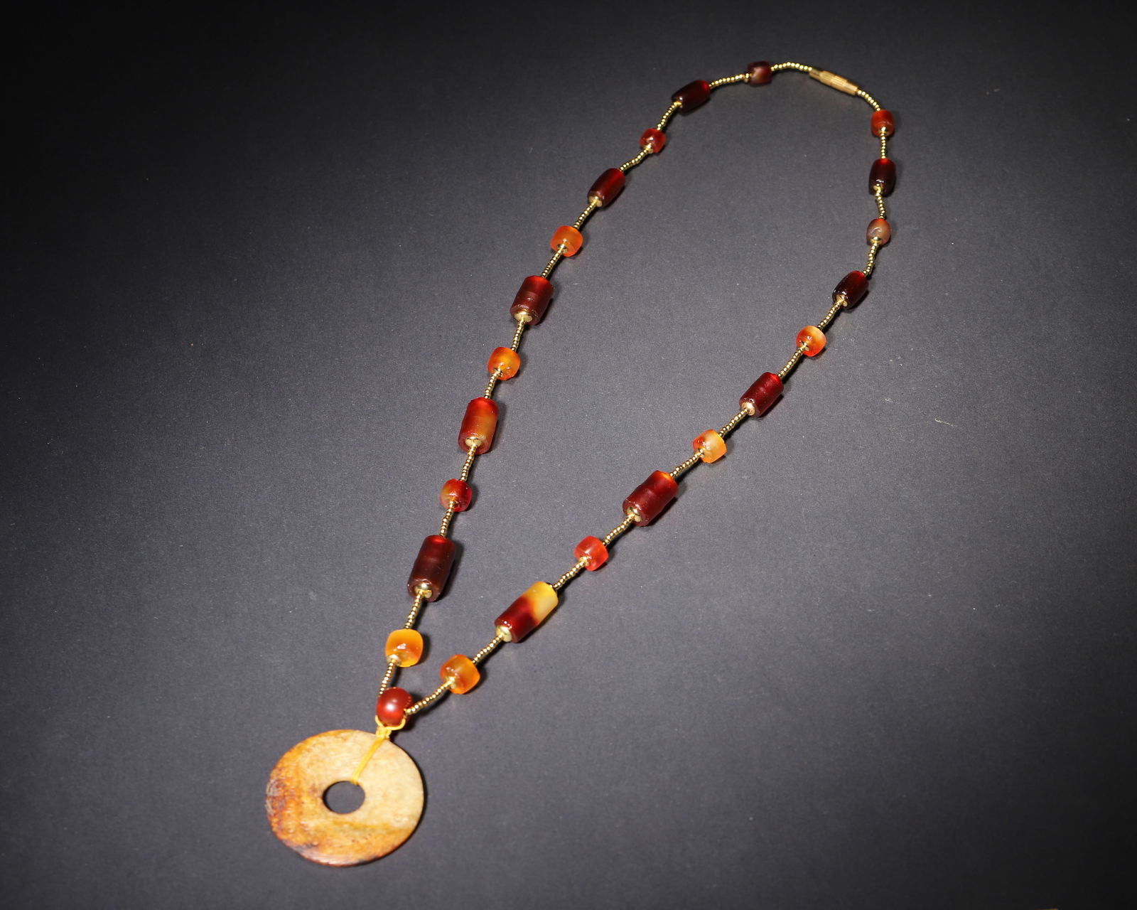 A chinese jade bi disc and agate bead necklace, spring and autumn period: Centered on a spring and autumn period jade bi disc with dense spiral patterns, this necklace is strung with archaic agate tubes, embodying the ritual and aesthetic of eastern zhou aristocratic adornm
