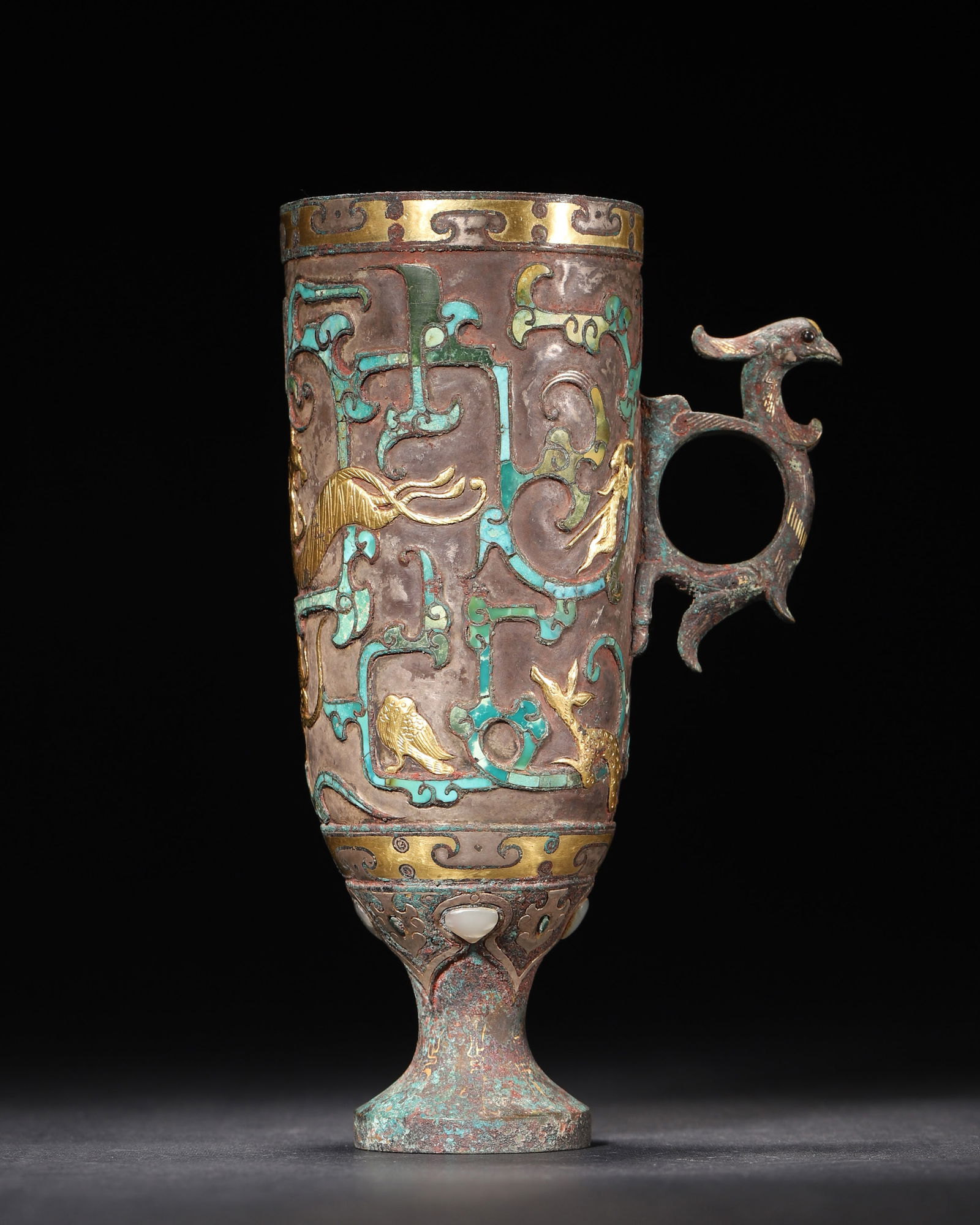 Warring states bronze cup with gold silver inlay, turquoise & jade: This warring states bronze cup features gold silver inlay, turquoise, and jade handle. Adorned with mythical beasts and feathered figures, its phoenix-shaped handle has inlaid beads. It exemplifies pr