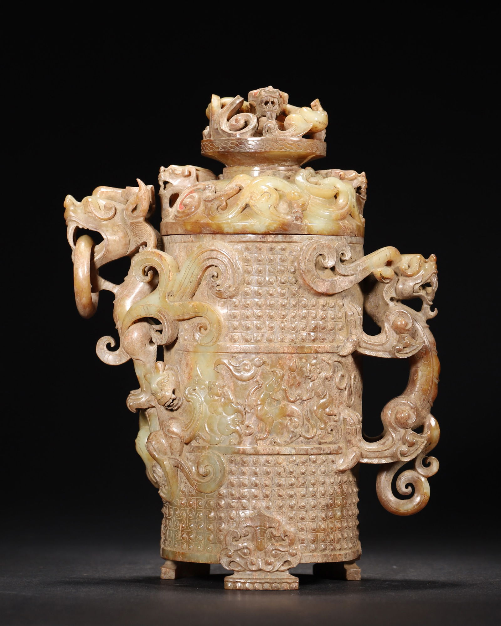 Han dynasty archaic jade covered hu vessel with patinated dragon patterns: Han dynasty archaic jade covered hu, made of patinated jade. The lid knob has openwork mythical beasts; The body is adorned with dragon patterns and dragon ring handles. Following shang-zhou ritual fo