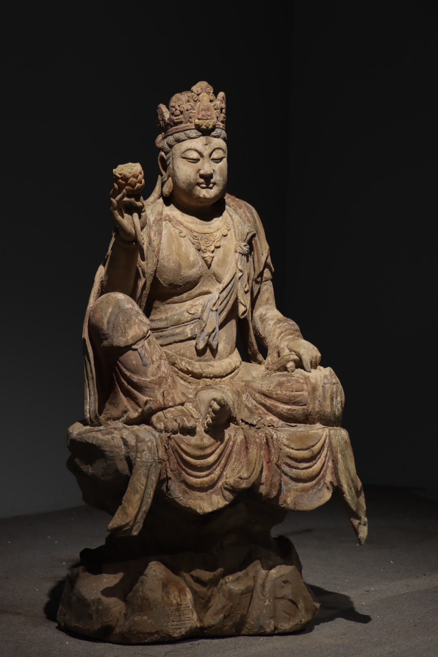 Song dynasty, nanmu wood painted seated guanyin holding a lotus: A song dynasty guanyin figure carved from nanmu wood with original polychromy. It features a compassionate expression, flowing drapery, a natural rock base, and a lotus held in one hand, embodying bot