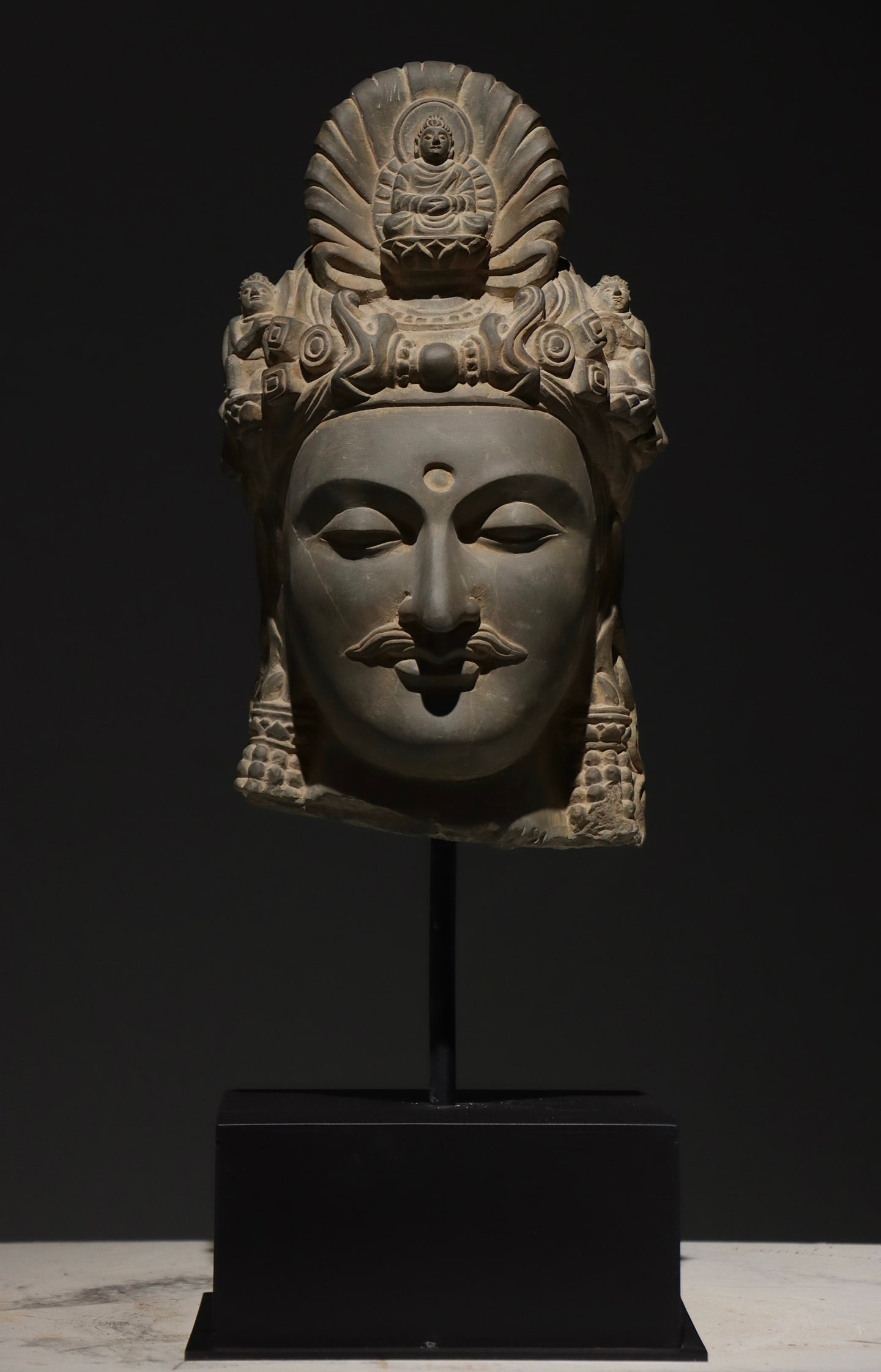 3Rd-4th century, gandhara schist bodhisattva head with buddha-in-crown: A late gandhara period bodhisattva head carved from schist, combining greek realism with buddhist iconography. It features an ornate crown with a seated buddha, serene expression, and urna. A vital re
