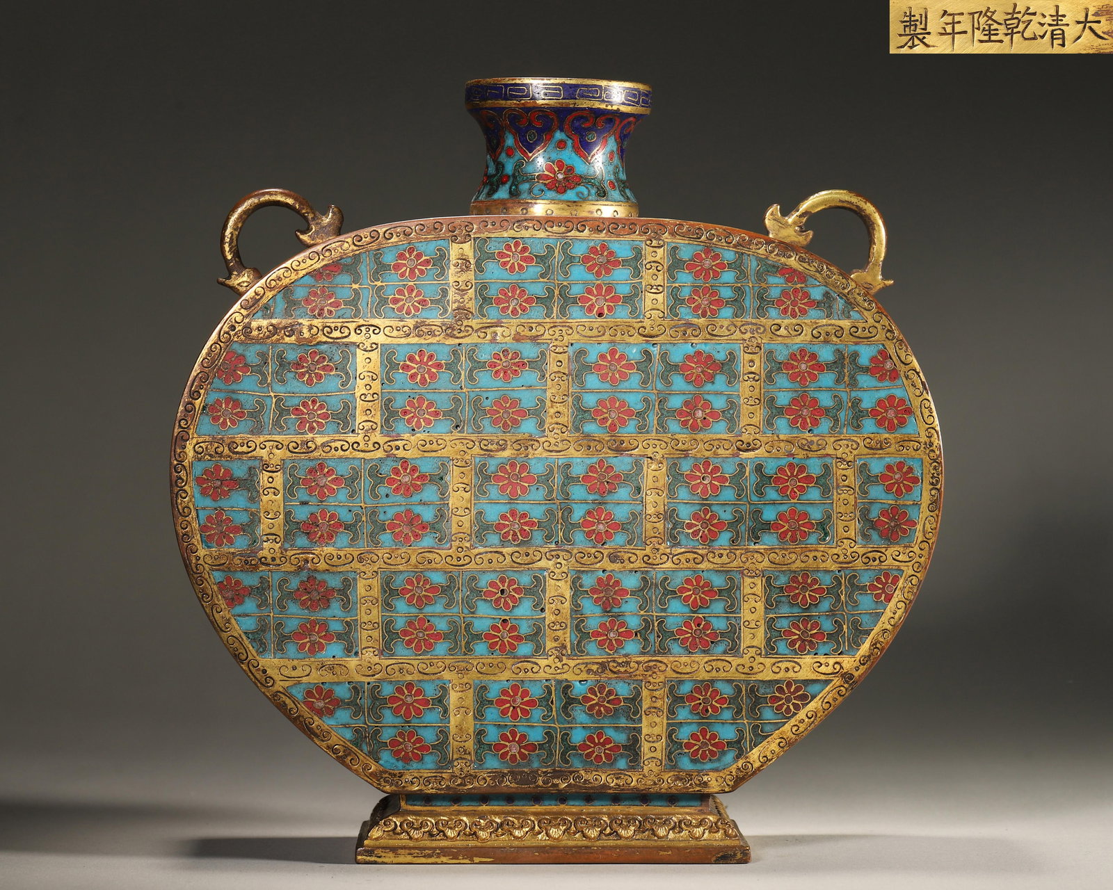 QING DYNASTY, QIANLONG IMPERIAL-MADE, CLOISONNÉ ENAMEL ON COPPER FLAT VASE WITH BROCADE GROUND: Width 22.0cm (8.66in), Height 23.0cm (9.06in), Weight 2335.0g (5.15lb)Copper body with gilding, flat round shape with double beast ears, peacock blue background decorated with regular brocade lattice