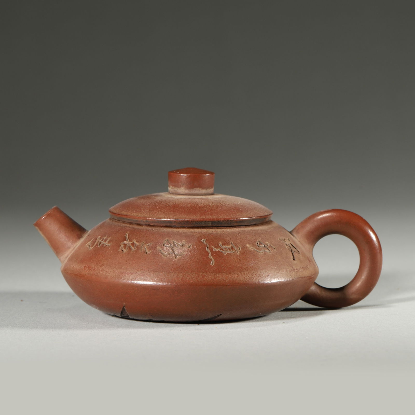 A FINE QING DYNASTY (19TH CENTURY) ZHUNI CLAY FLAT-ROUND TEAPOT WITH POEM AND BAMBOO CARVINGS: 4.33" x 3.15" x 1.97" inches (11.0 cm x 8.0 cm x 5.0 cm)This elegant Qing teapot is crafted from fine Zhuni clay, with delicate running-script poetic inscriptions and bamboo carvings. It exemplifies t