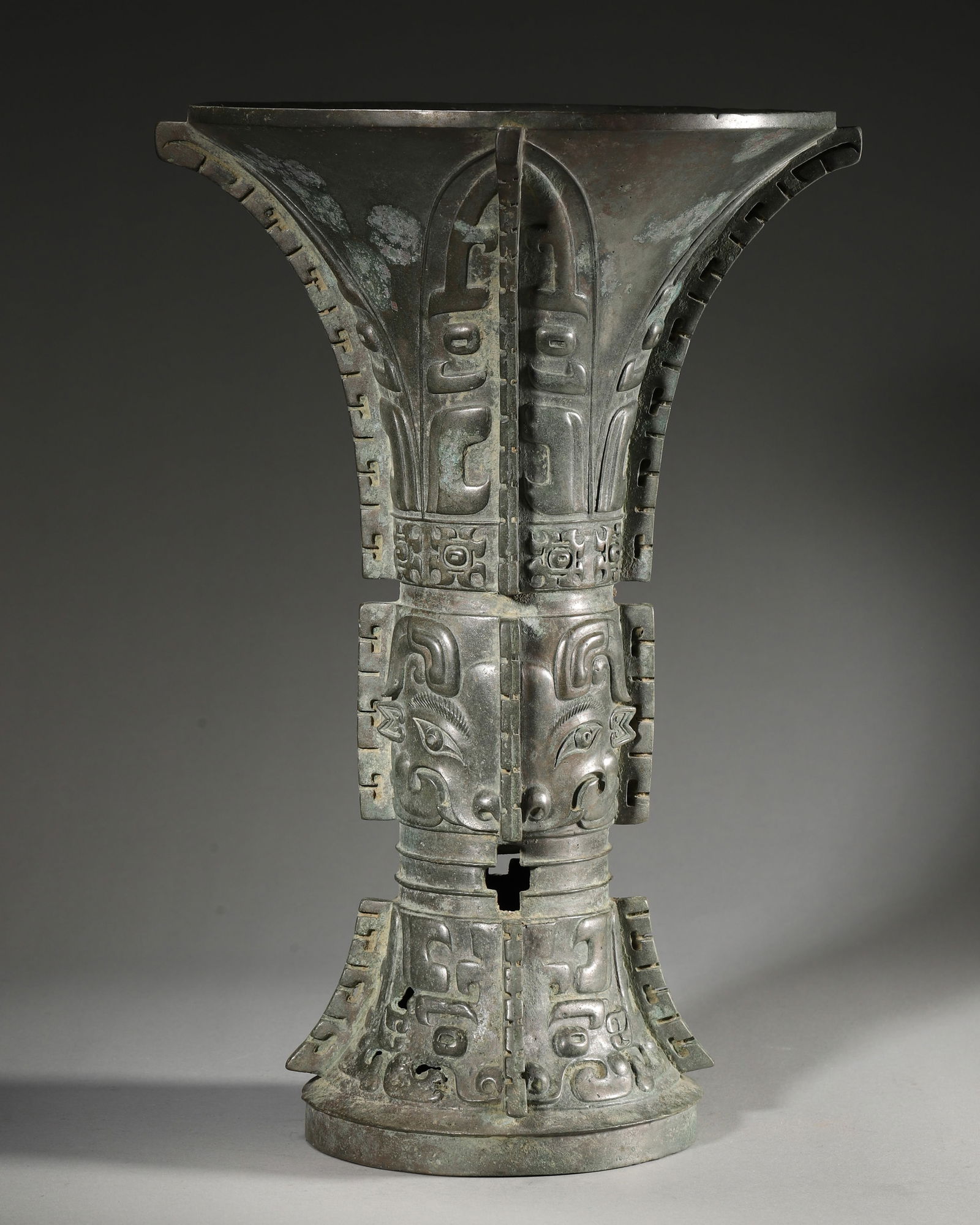 AN IMPORTANT ARCHAIC BRONZE RITUAL WINE VESSEL (GU), EARLY WESTERN ZHOU DYNASTY: D:24cm (9.45inches) H:35cm WT:4731g (10.43pounds)A fine archaic bronze ritual wine vessel (gu), Early Western Zhou dynasty, with prominent taotie masks, flanges, and an interior inscription, of excell