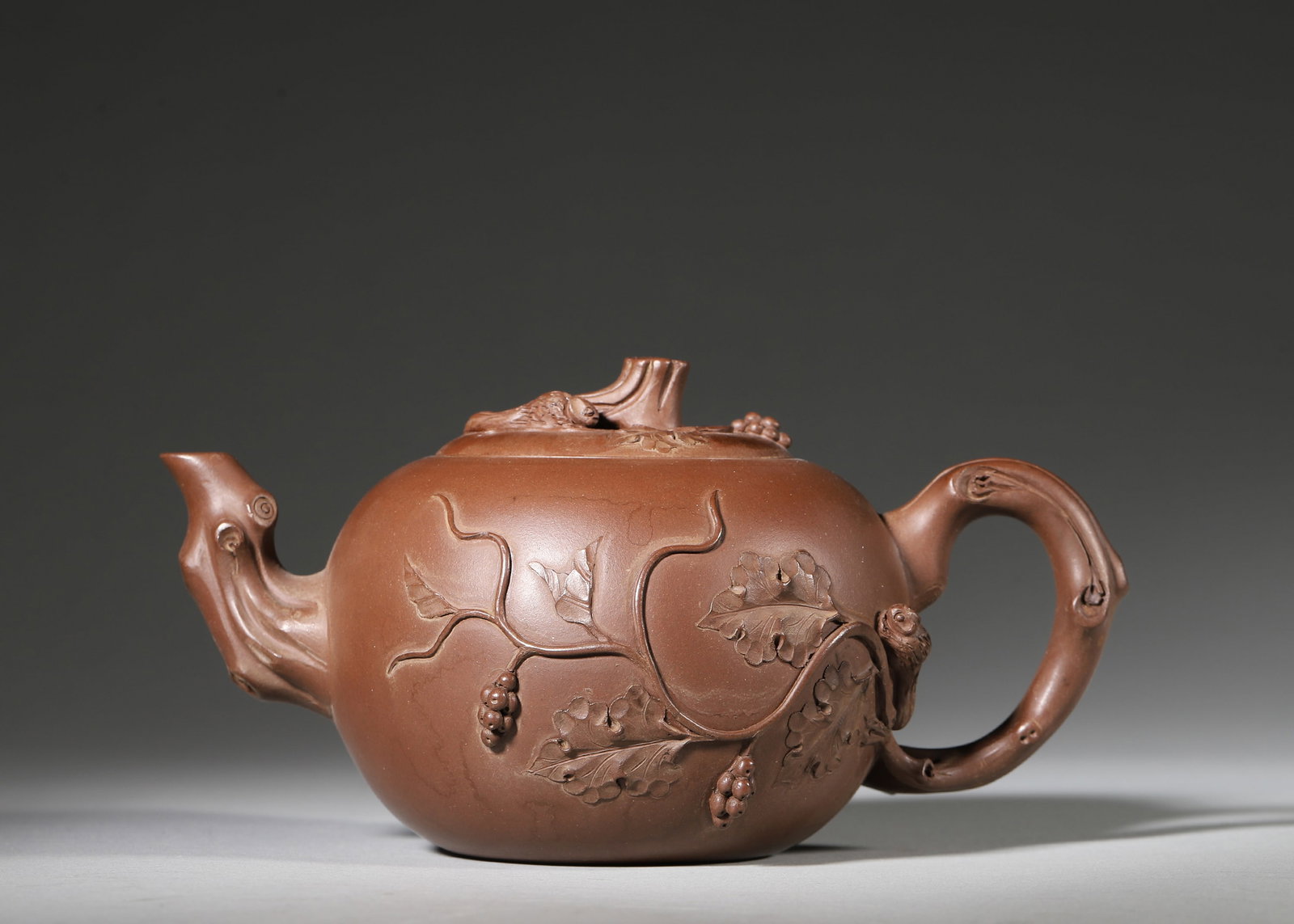 ZISHA TEAPOT WITH SQUIRREL AND GRAPE CARVING BY ZHU KEXIN: 7.09in x 4.33in x 3.54in (18.0cm x 11.0cm x 9.0cm)Crafted by master Zhu Kexin, this Zisha teapot features lifelike squirrel-and-grape relief carving. Made of premium purple clay, it embodies the pinna
