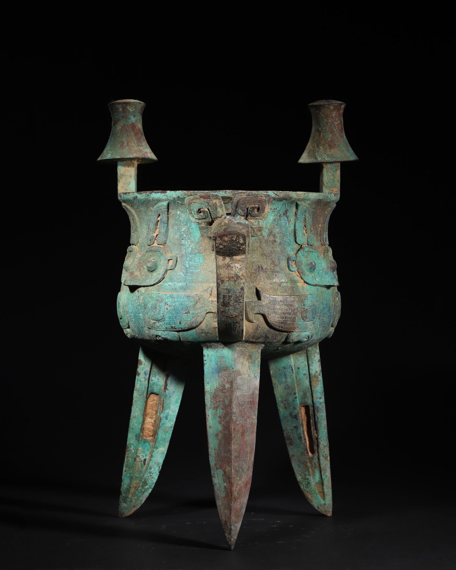 LATE SHANG DYNASTY BRONZE JIA VESSEL WITH OWL PATTERN AND UMBRELLA-SHAPED COLUMNS: 11.42in (29.0cm), 18.298lb (8300.0g)This Late Shang bronze jia features robust form, umbrella-shaped columns, and a beast-head handle. High-relief owl motifs against thunder-cloud patterns embody the