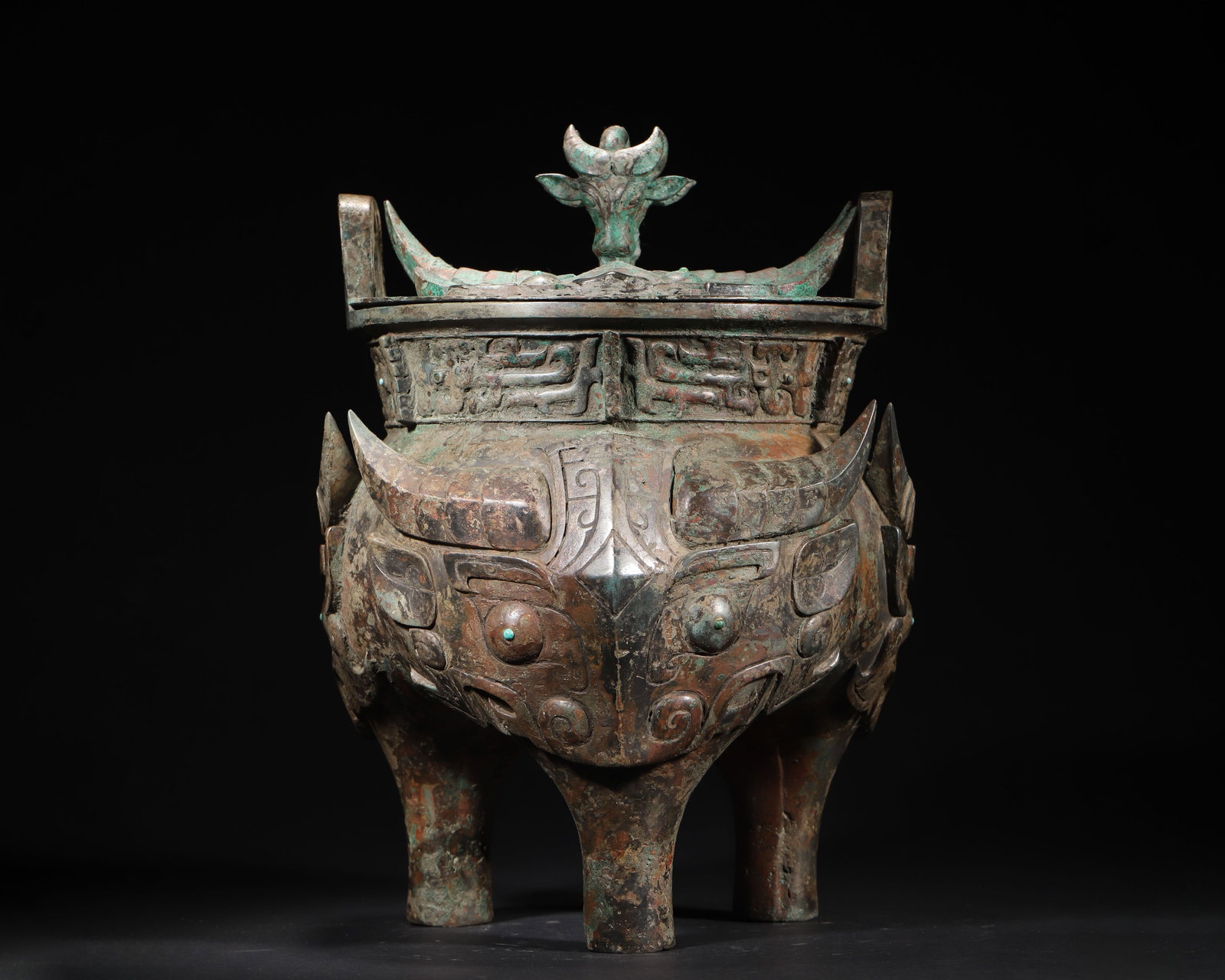EARLY WESTERN ZHOU DYNASTY BRONZE LI DING VESSEL WITH BEAST MASK PATTERN AND OX-HEAD LID: 9.45in (24.0cm), 18.658lb (8463.0g)This Early Western Zhou bronze li ding features a robust form with an ox-head finial on its lid. High-relief beast mask patterns, inlaid turquoise eyes, and dragon m
