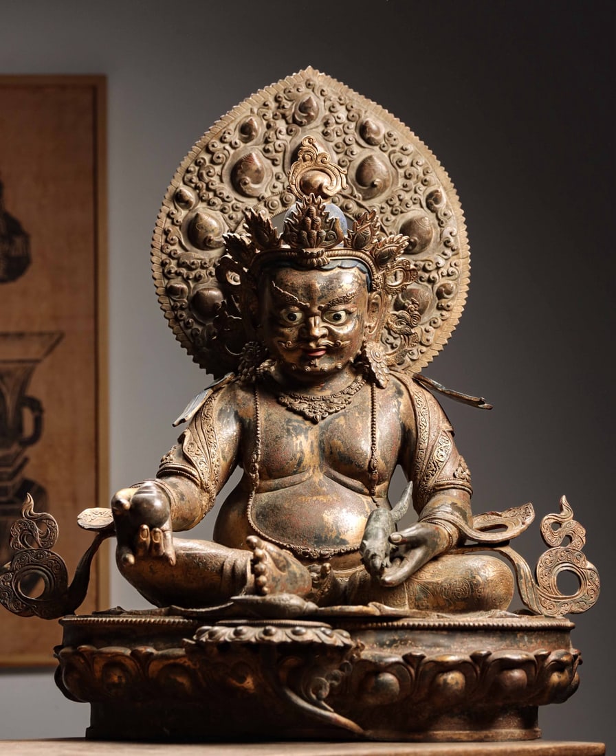 GILT-BRONZE FIGURE OF YELLOW JAMBHALA, 17TH-18TH CENTURY: 29.13" x 23.62" x 15.35" (74cm x 60cm x 39cm)| 62.28lb (28250g)A fine 17th-18th century Tibetan gilt-bronze figure of Yellow Jambhala, seated on a lotus base, holding a mongoose and a jewel, with a ma