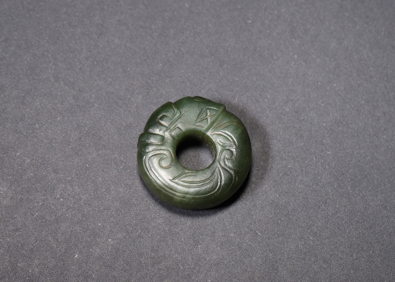 LATE SHANG DYNASTY GREEN JADE DRAGON-COILED BI-RING: 1.57" (4.0cm)A fine late Shang Dynasty (c.1600-1046 BC) green jade bi-ring, carved with a coiled dragon motif. Adorned with sharp double incised cloud and rhombus patterns, featuring the iconic "chen"