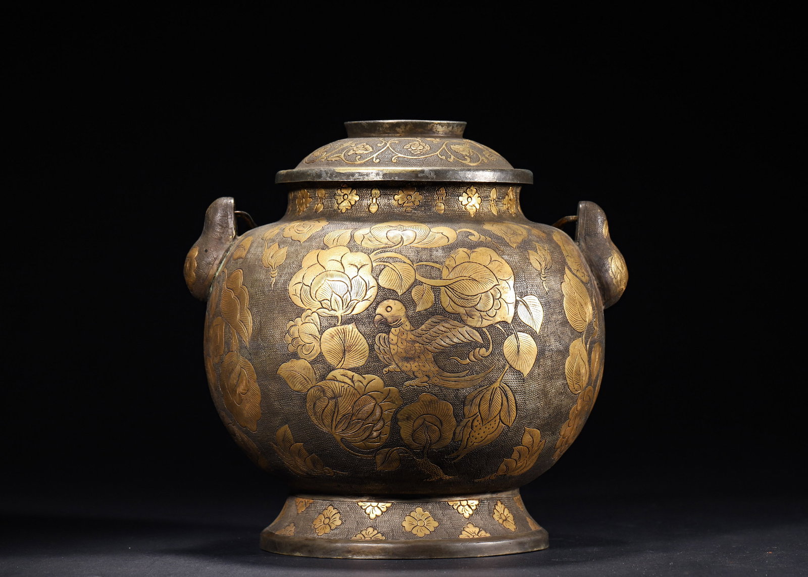 A FINE TANG DYNASTY GILT-SILVER JAR WITH BIRD-AND-FLOWER MOTIFS AND HANDLE: 7.87in x 7.48in (20.0cm x 19.0cm), 3.027lb (1373.0g)This Tang Dynasty gilt-silver jar is crafted with a fish-roe ground, intricately carved with parrot-and-peony motifs, and fitted with a gilt handle.