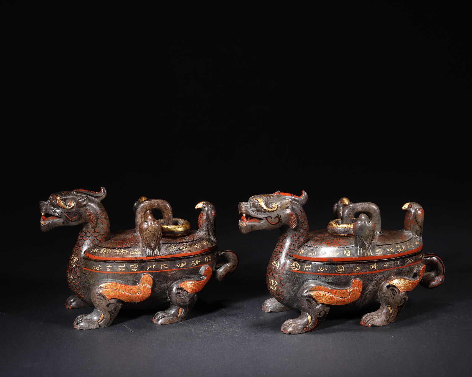 A PAIR OF FINE HAN DYNASTY DARK JADE INLAID GOLD AND CINNABAR 'MYTHICAL BEAST' VESSELS AND COVERS: 7.09in x 3.54in x 3.94in (18.0cm x 9.0cm x 10.0cm), 3.508lb (1591.0g)This pair of Han Dynasty vessels, carved from dark jade, features intricate gold-inlaid inscriptions and cinnabar highlights. Shape