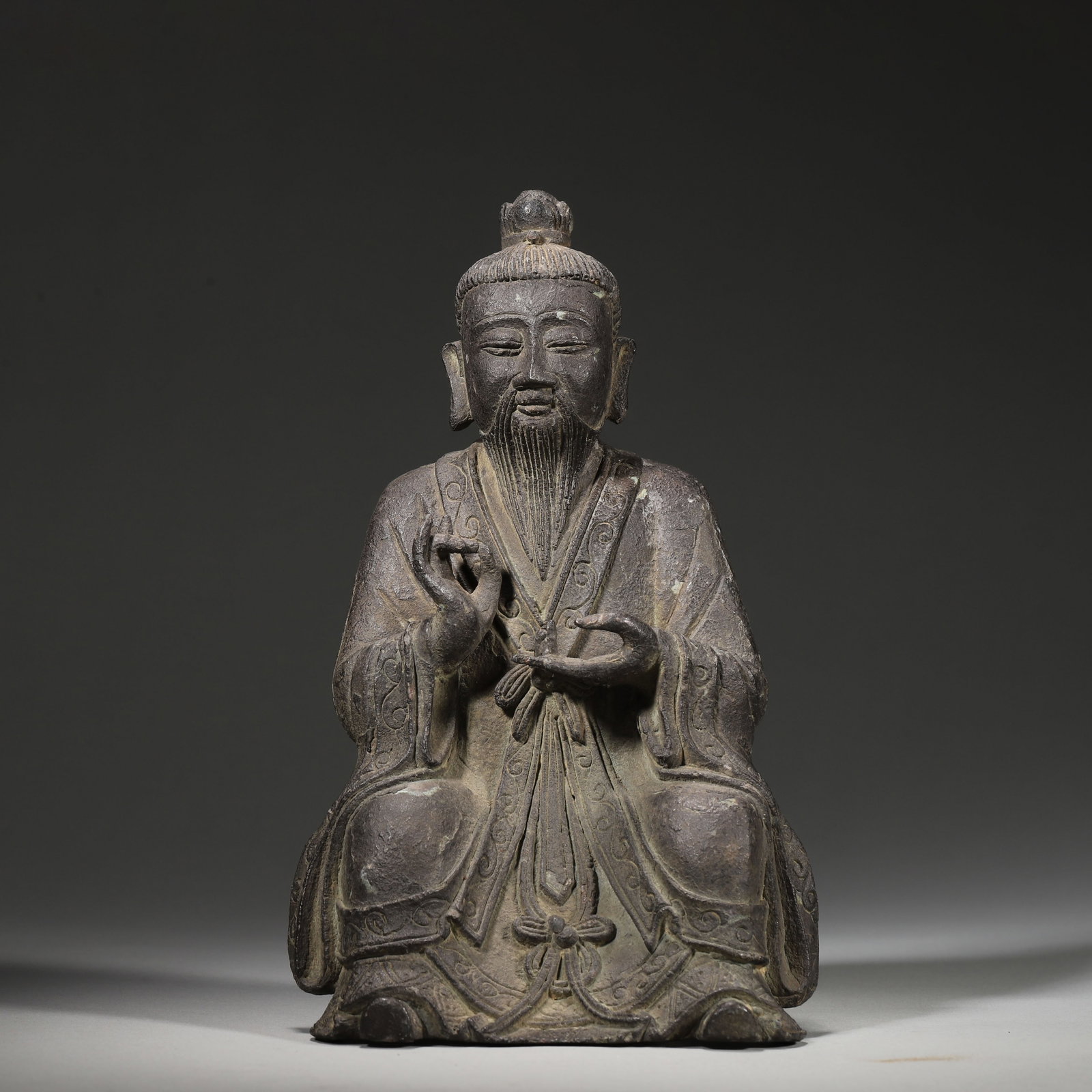 A Bronze Seated Taoist Figure, Ming Dynasty: W 12cm (4.72 in); H 20cm (7.87 in); Wt 997g (2.2 lb)A Ming Dynasty bronze seated Taoist figure, with a serene face, long beard, wearing a Taoist robe with carved drapery, and hands in ritual gesture. 