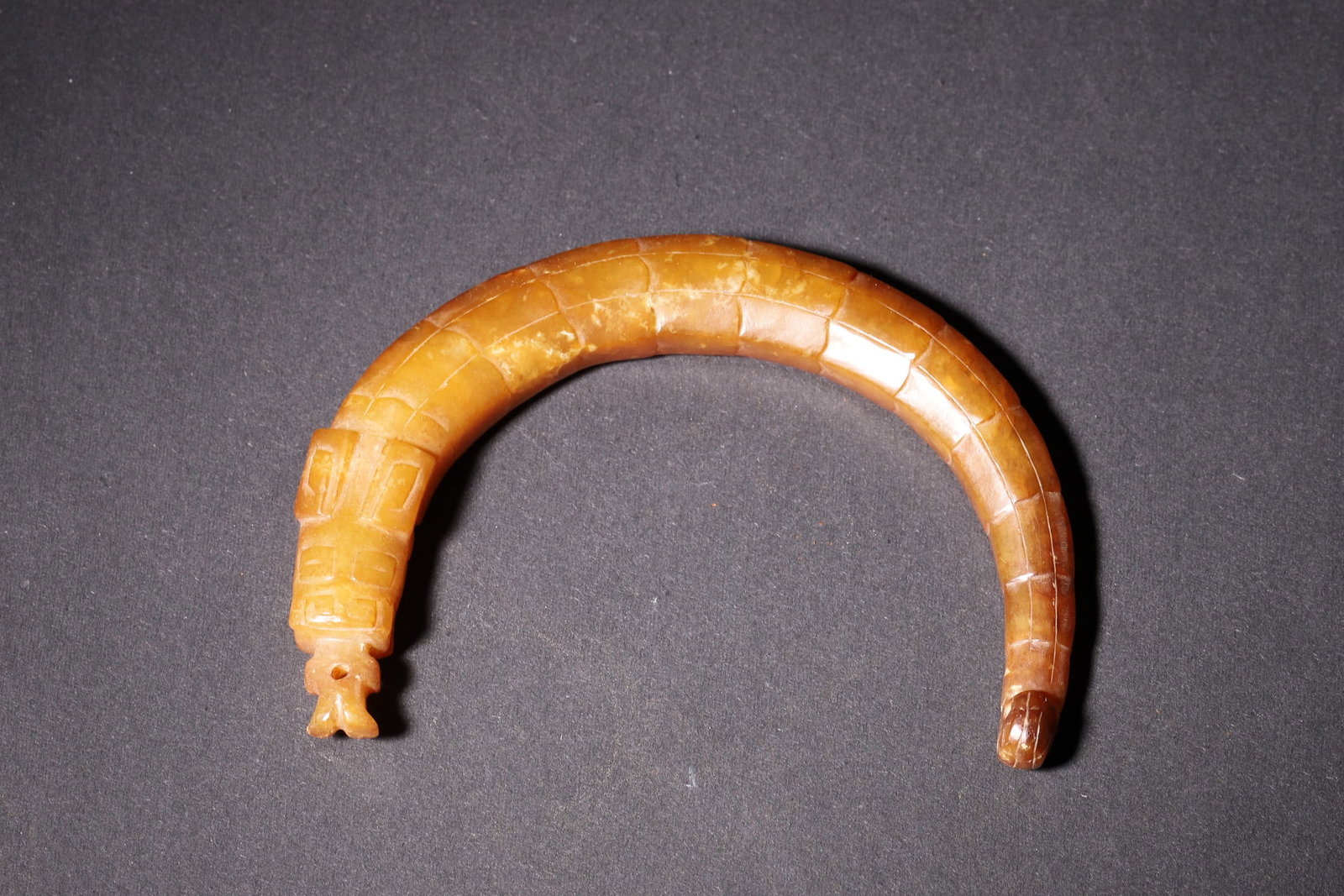 A Shang Dynasty Hetian Jade Dragon-Shaped Huang with Deity Pattern: Length 9.5cm (3.74in), Width 7.2cm (2.83in), Weight 51.0g (0.11lb)A Shang Dynasty Hetian jade dragon-shaped huang, carved with deity pattern at one end and dragon head at the other. With natural russe