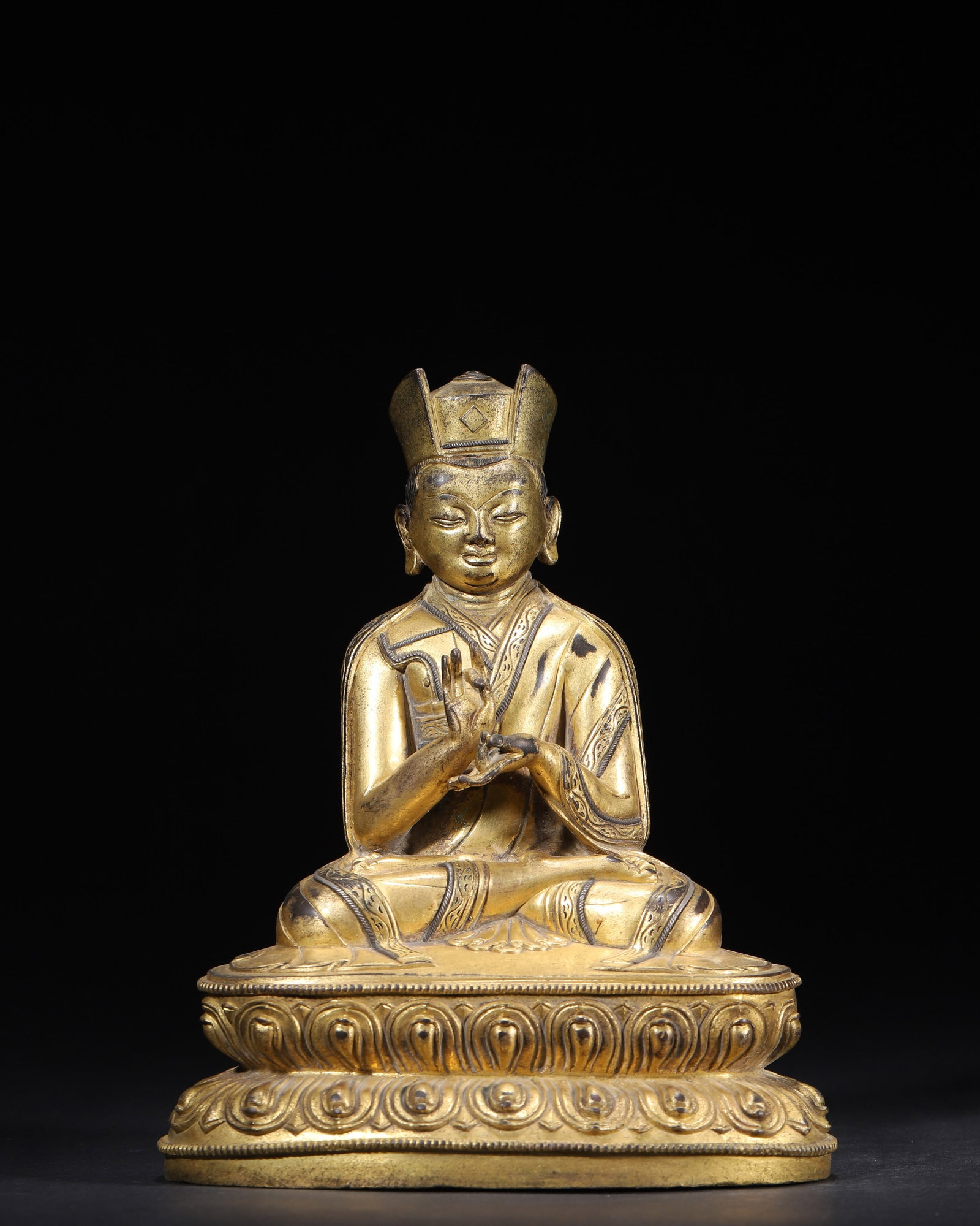 A Gilt-Bronze Figure of a Lama, Qing Dynasty: 1470.0 g (3.24 lb) | 13.0 x 9.0 x 17.0 cm (5.12 x 3.54 x 6.69 in)This is a fine Qing Dynasty Tibetan gilt-bronze lama figure, seated in lotus position with a monastic hat, hands in mudra, flowing robe