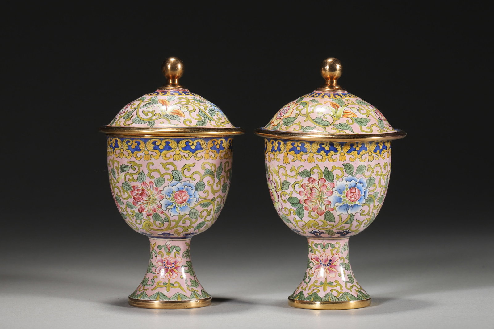 A Pair Of Enameled Copper Stem Cups With Floral Scrolls, Qianlong Period: 4.5cm x 9.5cm,64.0g (1.77in x 3.74in,WT 0.1411lb)A pair of imperial stem cups with copper bodies and pink enamel grounds. Painted with interlocking flowers and gilded borders, bearing a "Qianlong" mar