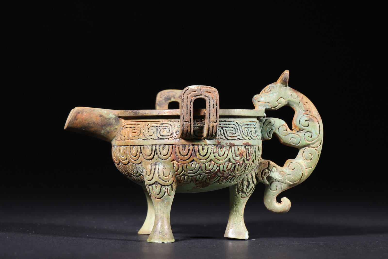 A Bronze Yi Vessel with Dragon Motifs - Western Zhou Dynasty: Length 13.0cm (5.12in), Width 9.0cm (3.54in), Height 8.5cm (3.35in), Weight 286.0g (0.63lb)This Western Zhou Dynasty bronze yi vessel features a spout, a dragon-shaped handle, and three legs,