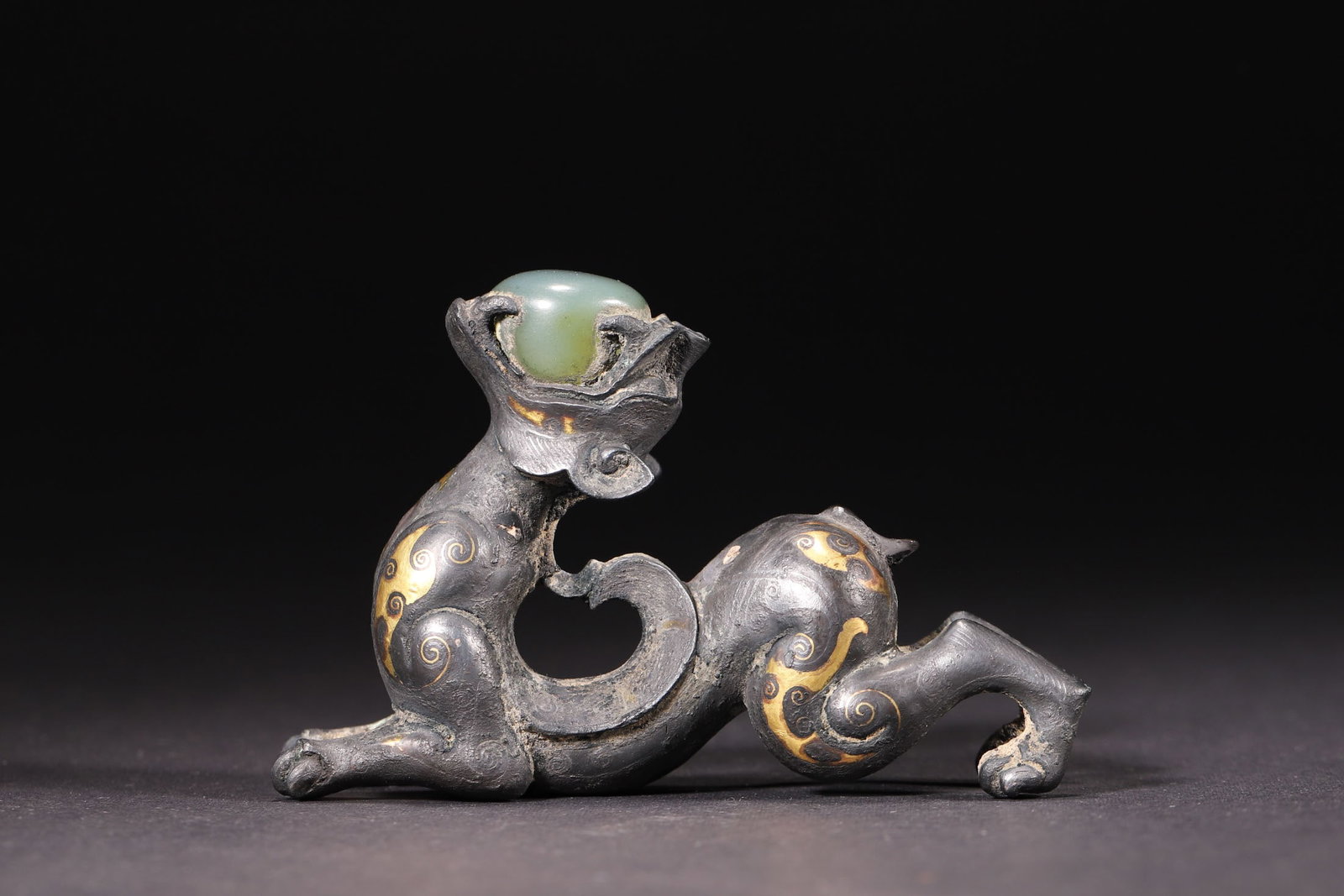 A Han Dynasty Bronze Beast Paperweight with Gold Inlay and Jade Inlay: Length 9.0cm (3.54in), Width 2.5cm (0.98in), Height 5.8cm (2.28in), Weight 268.0g (0.59lb)A Han Dynasty bronze beast paperweight, decorated with gold inlaid scroll patterns and inlaid with Hetian jade