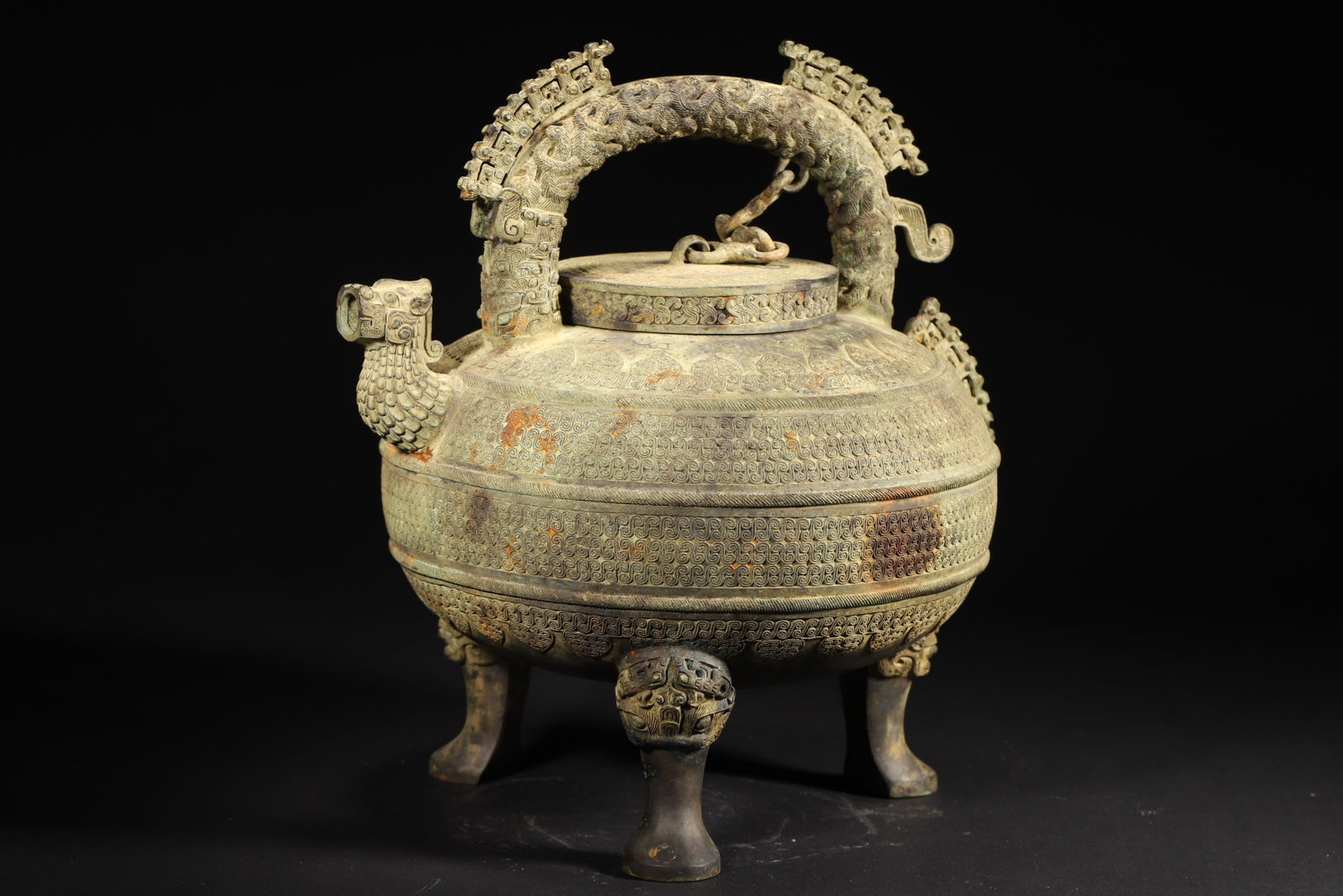 A Bronze He Vessel with Interlaced Chi-Dragon Patterns and Carry Handle, Warring States Period: 5605.0 g (12.36 lb) | 30.0 x 26.0 x 31.0 cm (11.81 x 10.24 x 12.2 in)This Warring States bronze he vessel features a robust and round shape with a beast-head spout and an arched carry handle adorned w