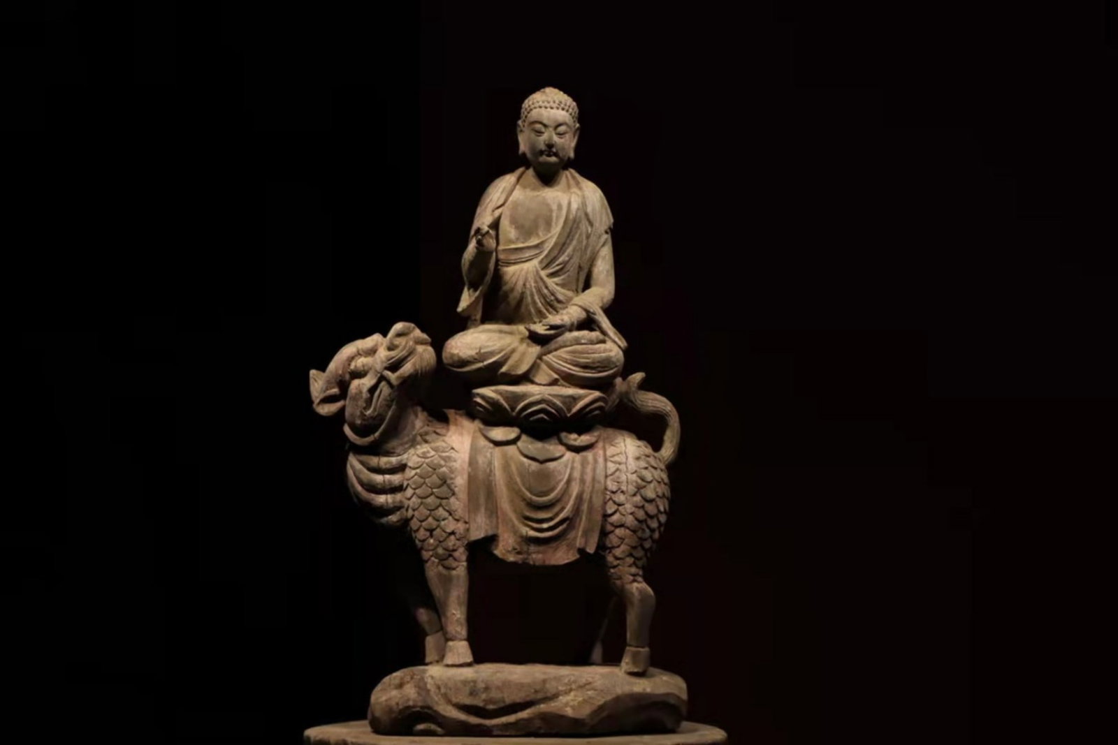 A Polychrome Wood Figure of Buddha Sakyamuni Seated on a Qilin - Ming Dynasty: Total Height 60cm (23.62 in)This polychrome wood figure of Buddha Sakyamuni seated on a qilin dates to the Ming Dynasty. The serene Buddha sits in meditation on a lotus throne atop the mythical beast,